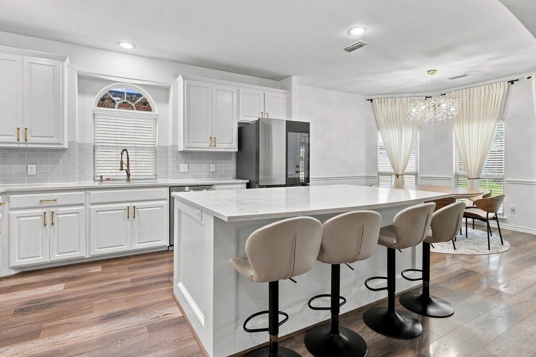 White cabinetry with gold-tone hardware, a center island with a stone countertop, wood-finish flooring, a tile backsplash, and recessed lighting