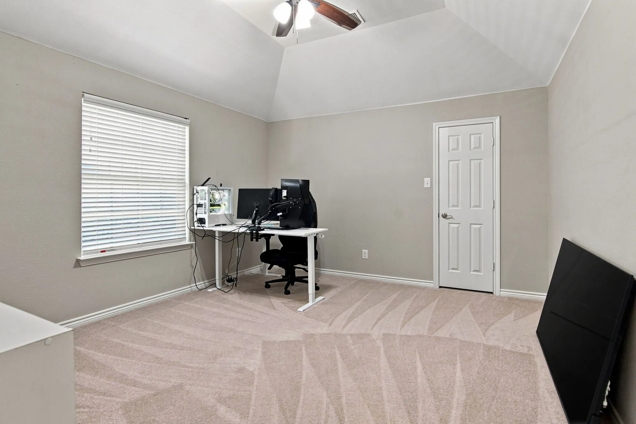 Vaulted ceiling, ceiling fan with integrated lighting, window with blinds, paneled interior door, and neutral-toned carpeting