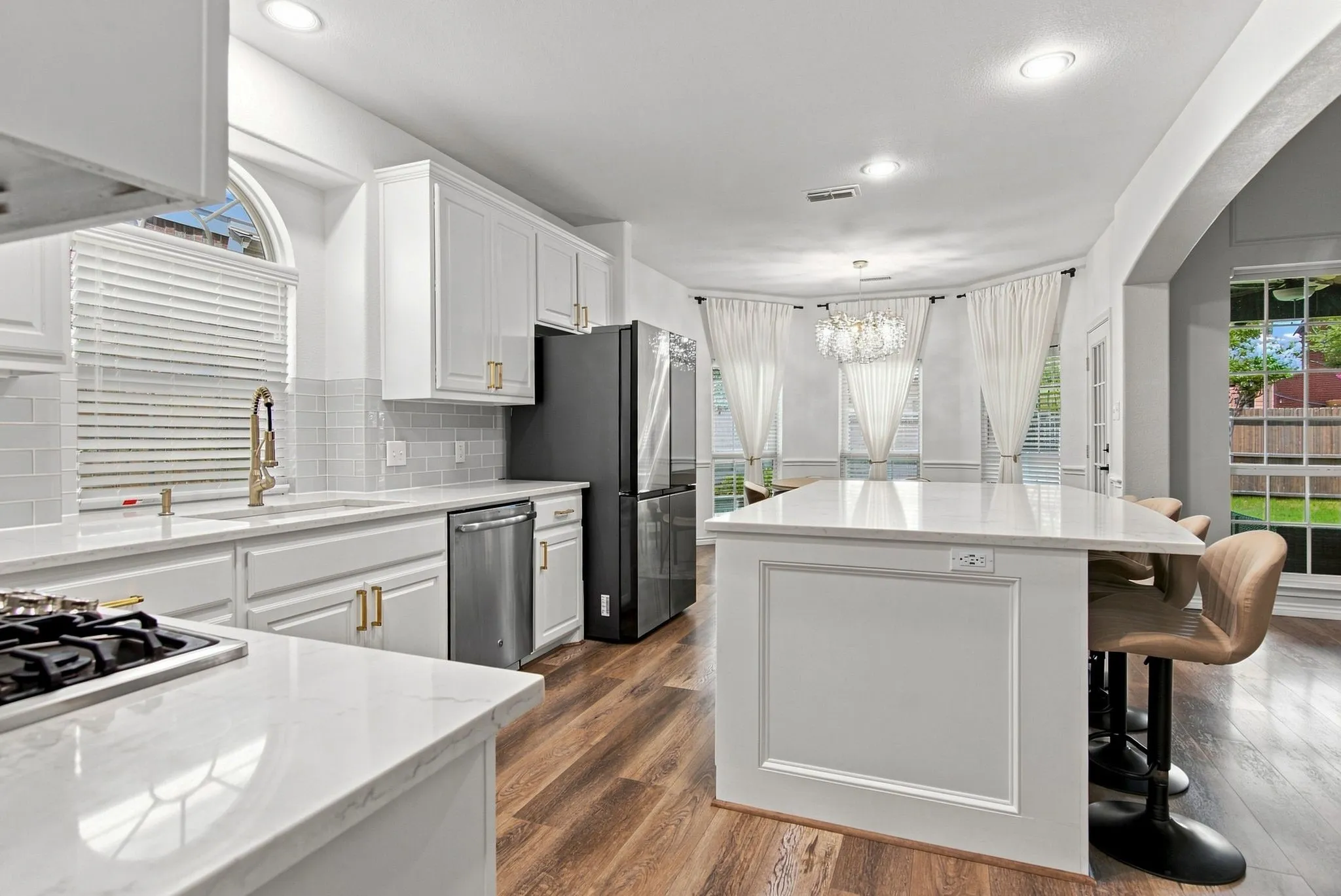 White cabinetry with gold-finish hardware, stainless steel appliances, wood-finish flooring, white countertop surfaces, and a decorative island with paneling