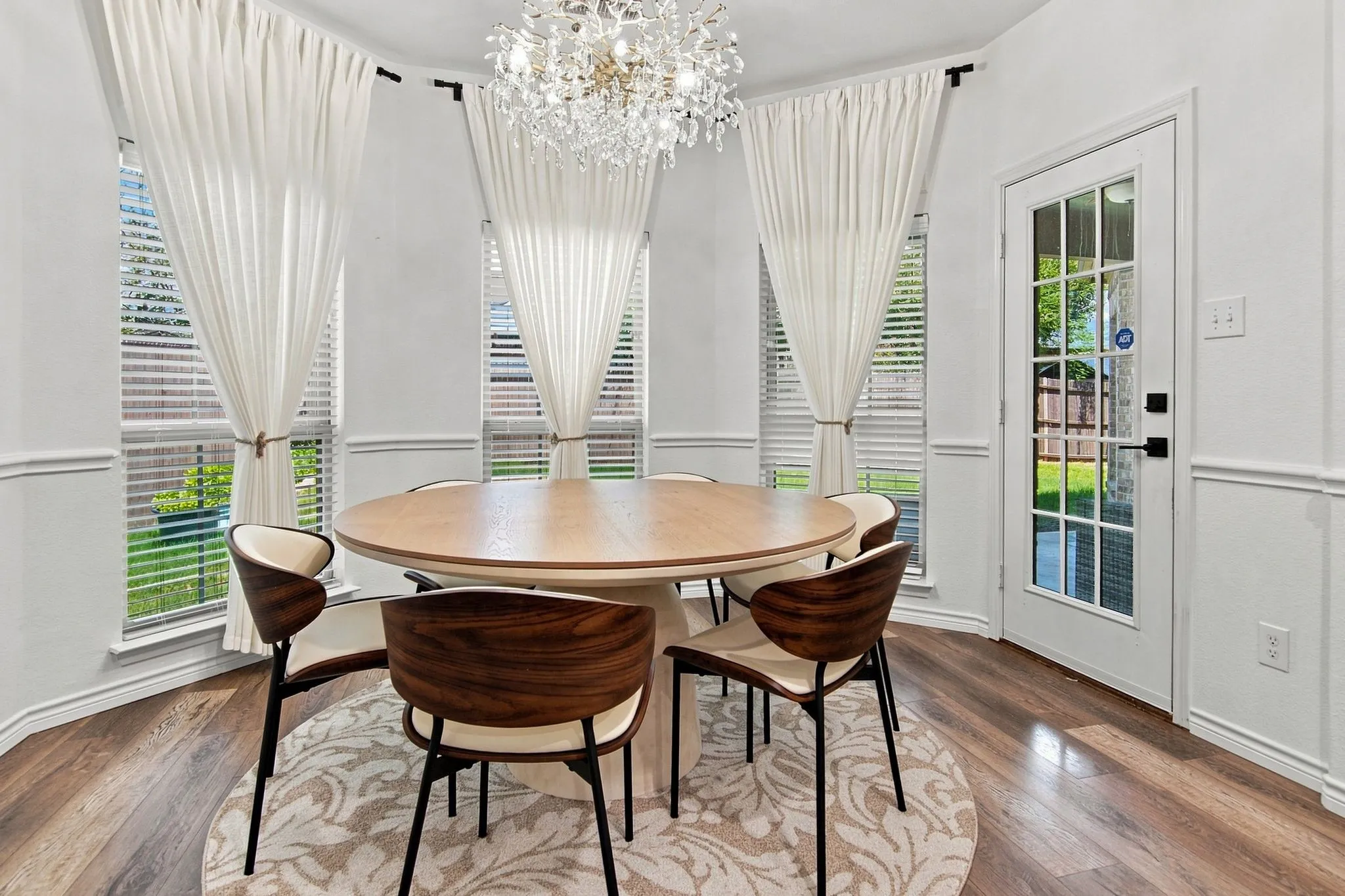 Bay window with multiple large windows, wood-finish flooring, white paneled door with glass inserts, and a crystal chandelier
