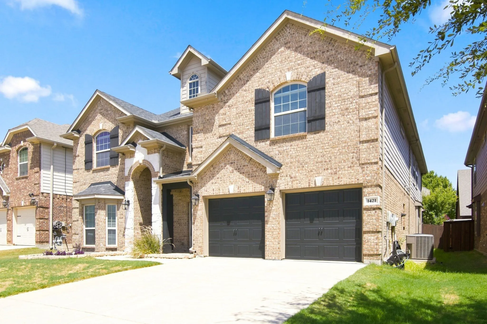 Brick exterior with dark shutters, arched entry, two-car garage, and dormer windows