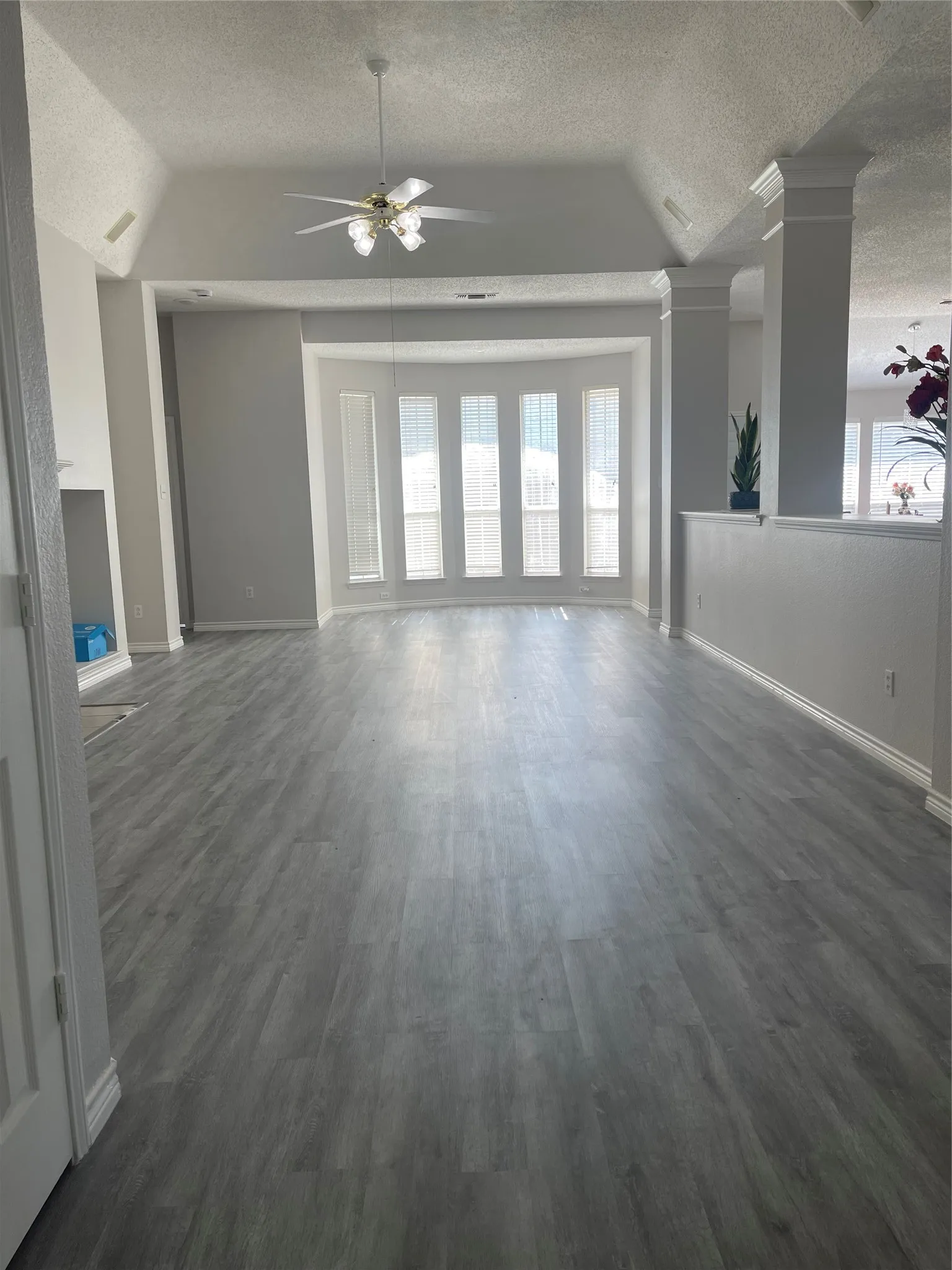 Spacious living area featuring wood-finish flooring, vaulted ceilings, a ceiling fan with integrated lighting, and a bay window