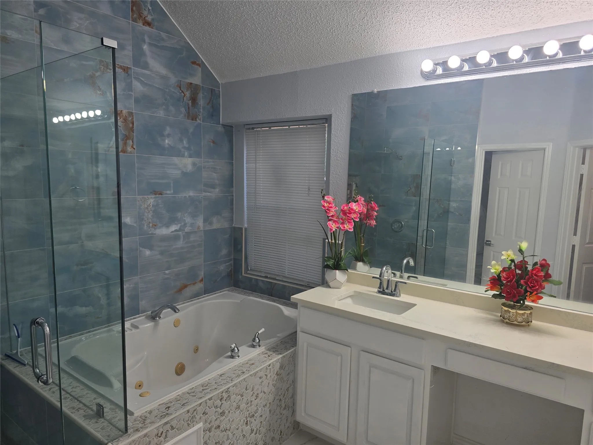 Blue tiled shower with clear glass enclosure and built-in jetted tub