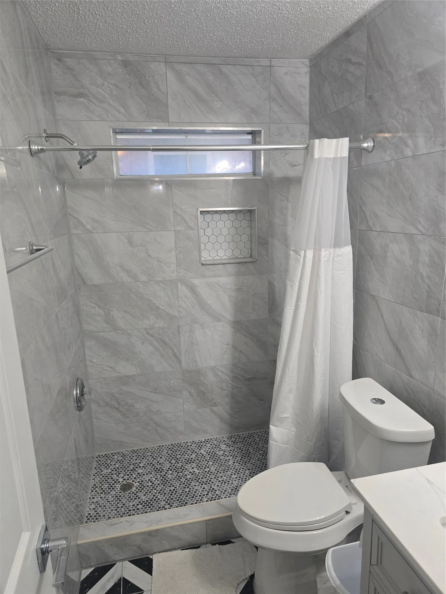 Shower with full-height tile surround, mosaic tile shower pan, and built-in shower niche