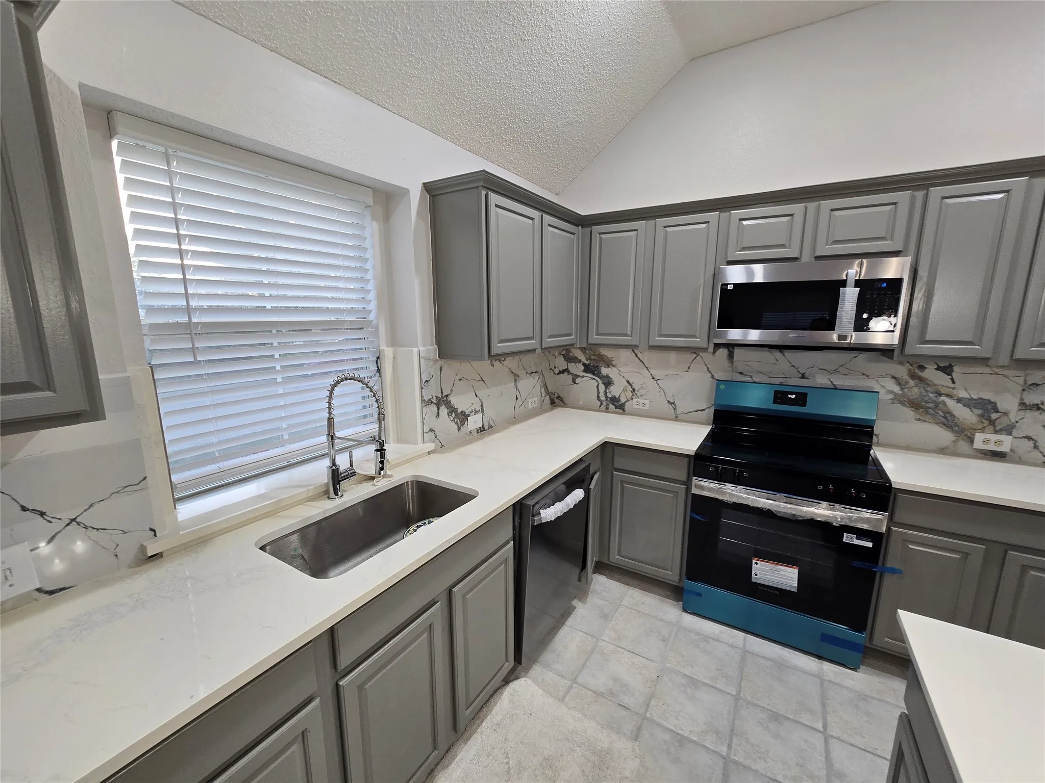 Kitchen featuring gray cabinetry, white countertops, marble-patterned backsplash, stainless steel sink with a gooseneck faucet, and tile flooring