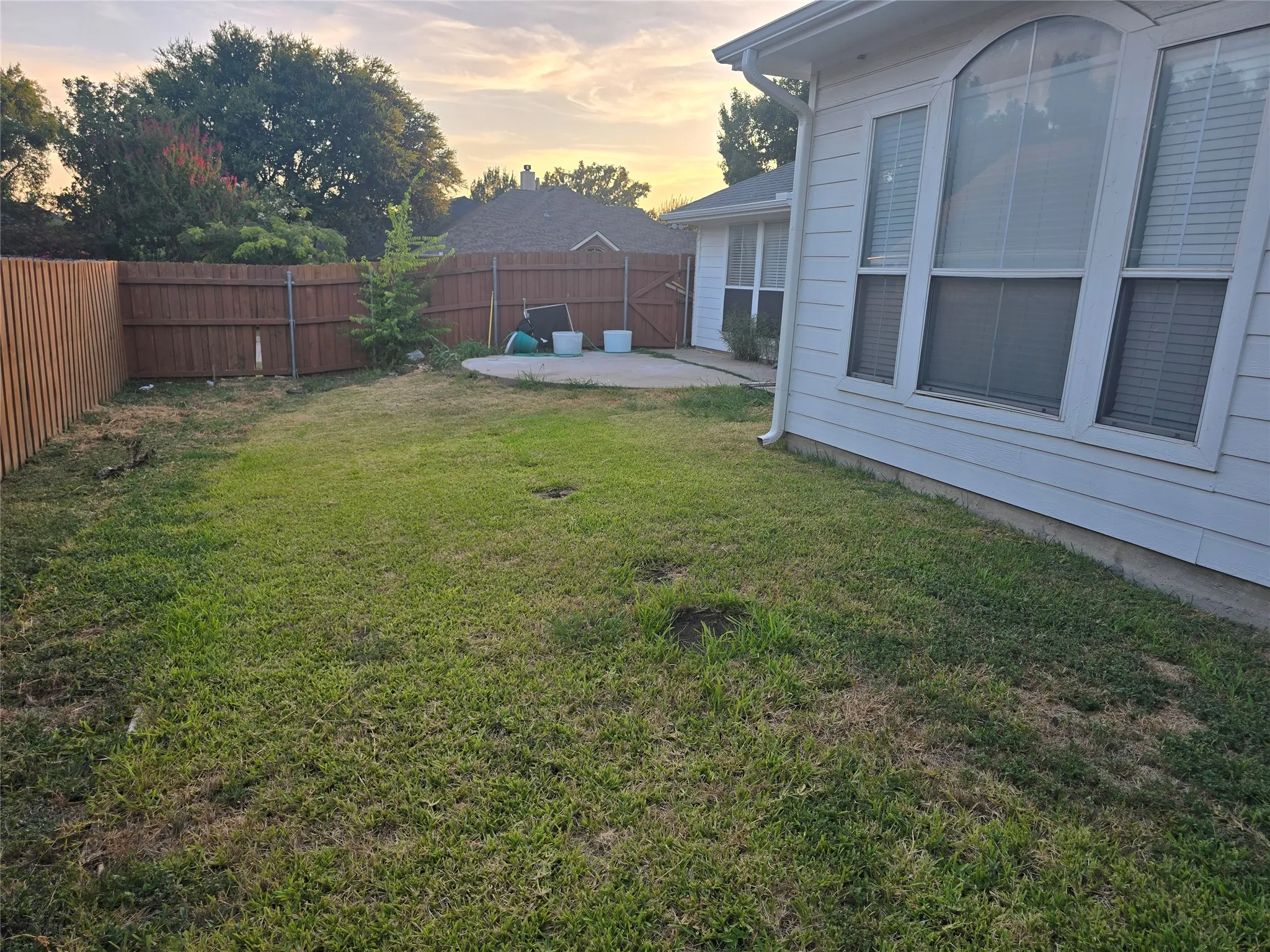 Fenced backyard featuring a concrete patio, exterior siding, and multiple windows with an arched transom