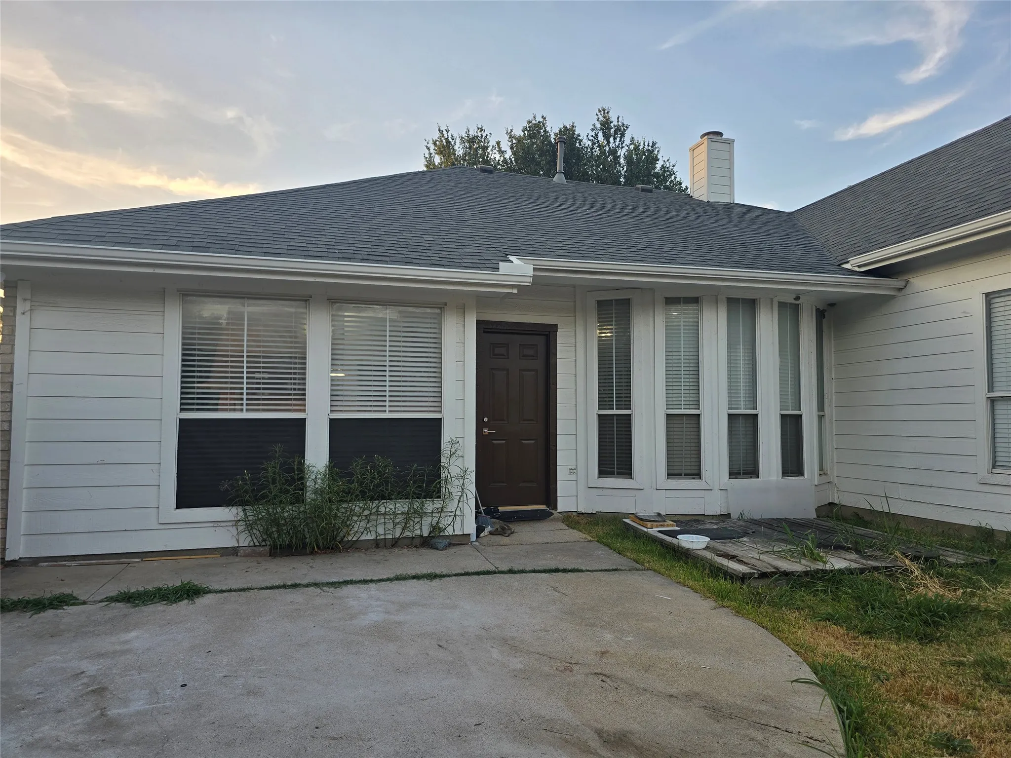 White siding exterior with a dark brown entry door, multiple windows, and an asphalt shingle roof