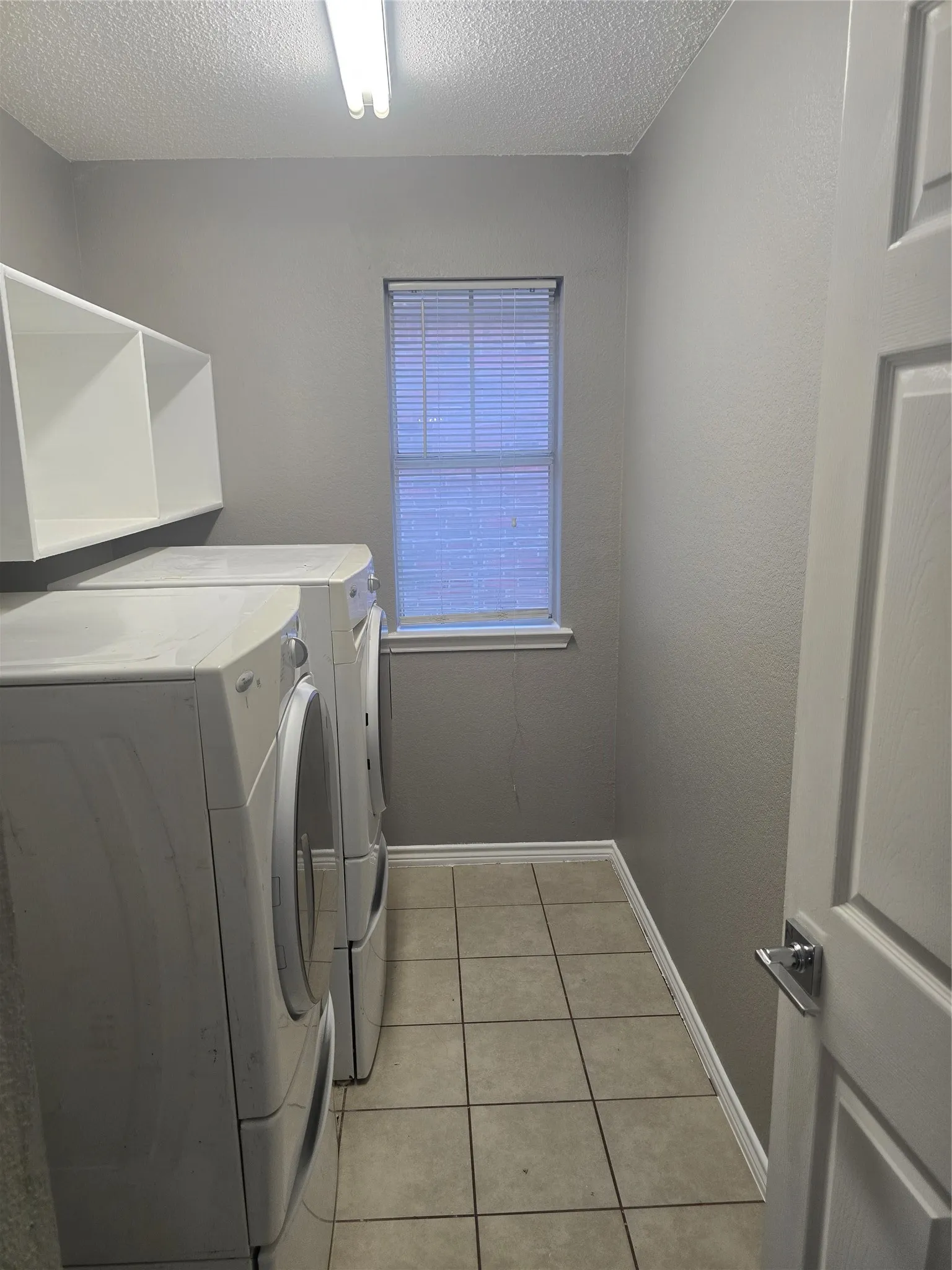 Laundry area featuring neutral wall paint, tiled flooring, built-in shelving, and a window with blinds