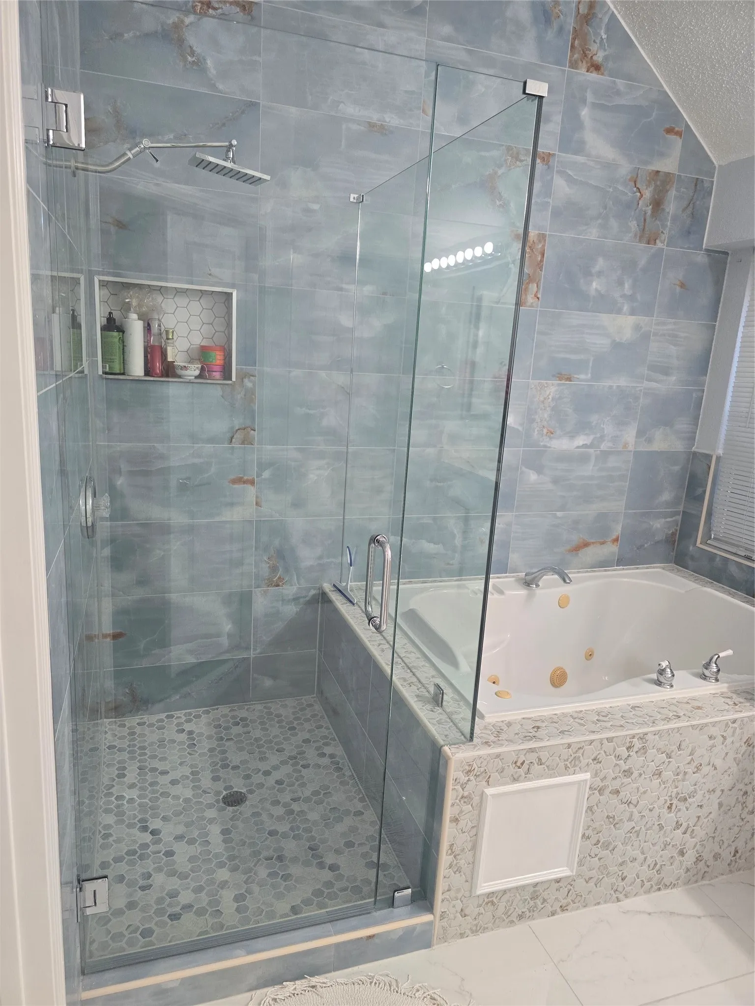 Glass-enclosed shower with a rainfall showerhead, tiled niche, and hexagonal floor tiles