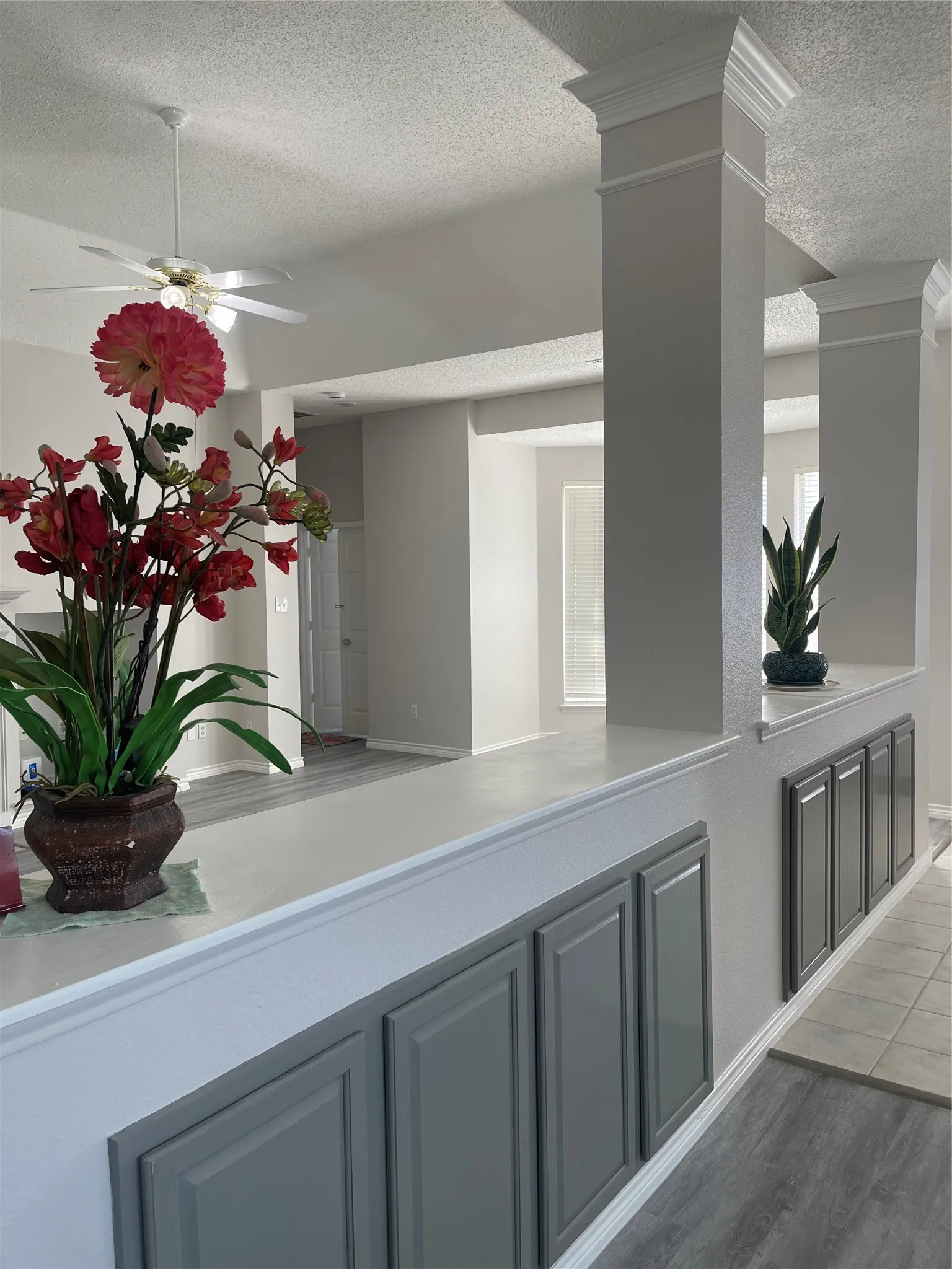 Interior half-wall with integrated cabinetry, decorative columns, wood-finish flooring, and a ceiling fan