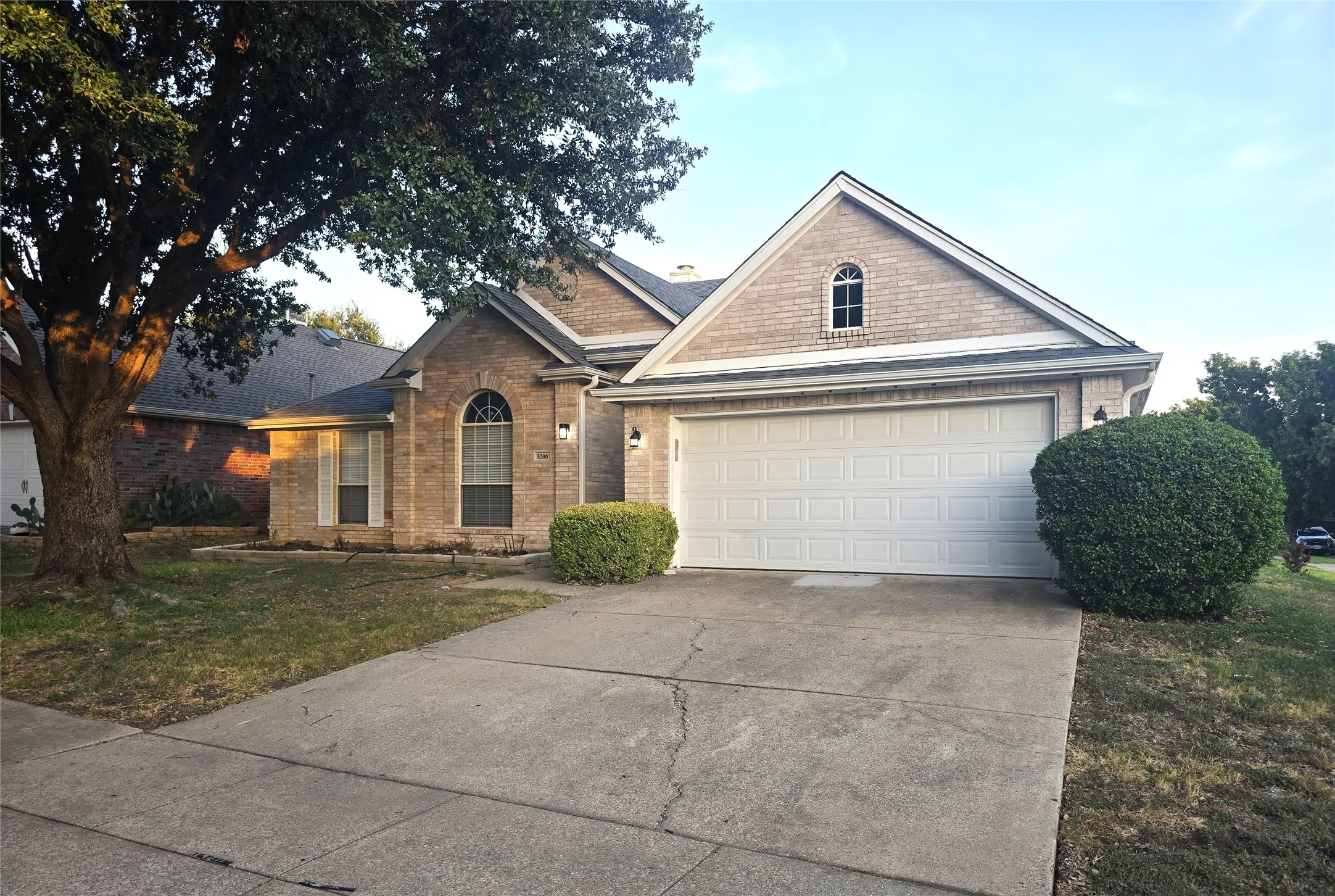 Brick exterior with gabled roofline, arched window, attached garage, and concrete driveway