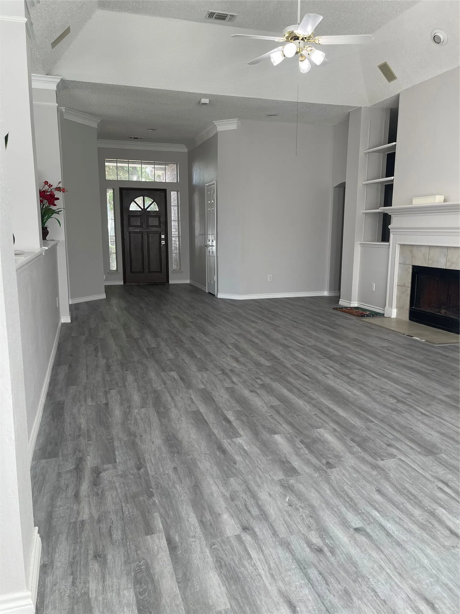 Vaulted ceiling, wood-finish flooring, built-in shelving, decorative fireplace surround, and ceiling fan with integrated lighting
