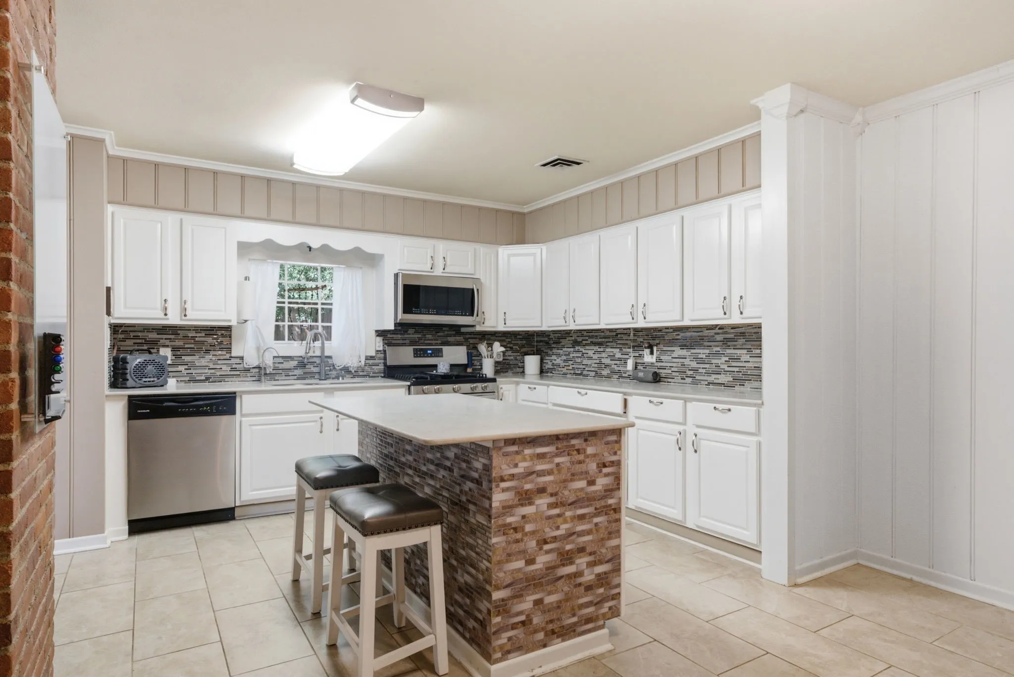 White cabinetry, stainless steel appliances, tile flooring, stone-clad kitchen island, and a mosaic tile backsplash