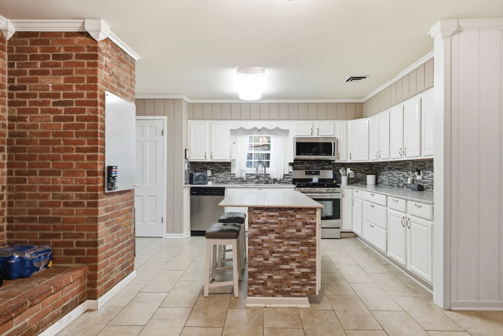 Kitchen featuring white cabinetry, stainless steel appliances, a mosaic tile backsplash, and a tiled kitchen island