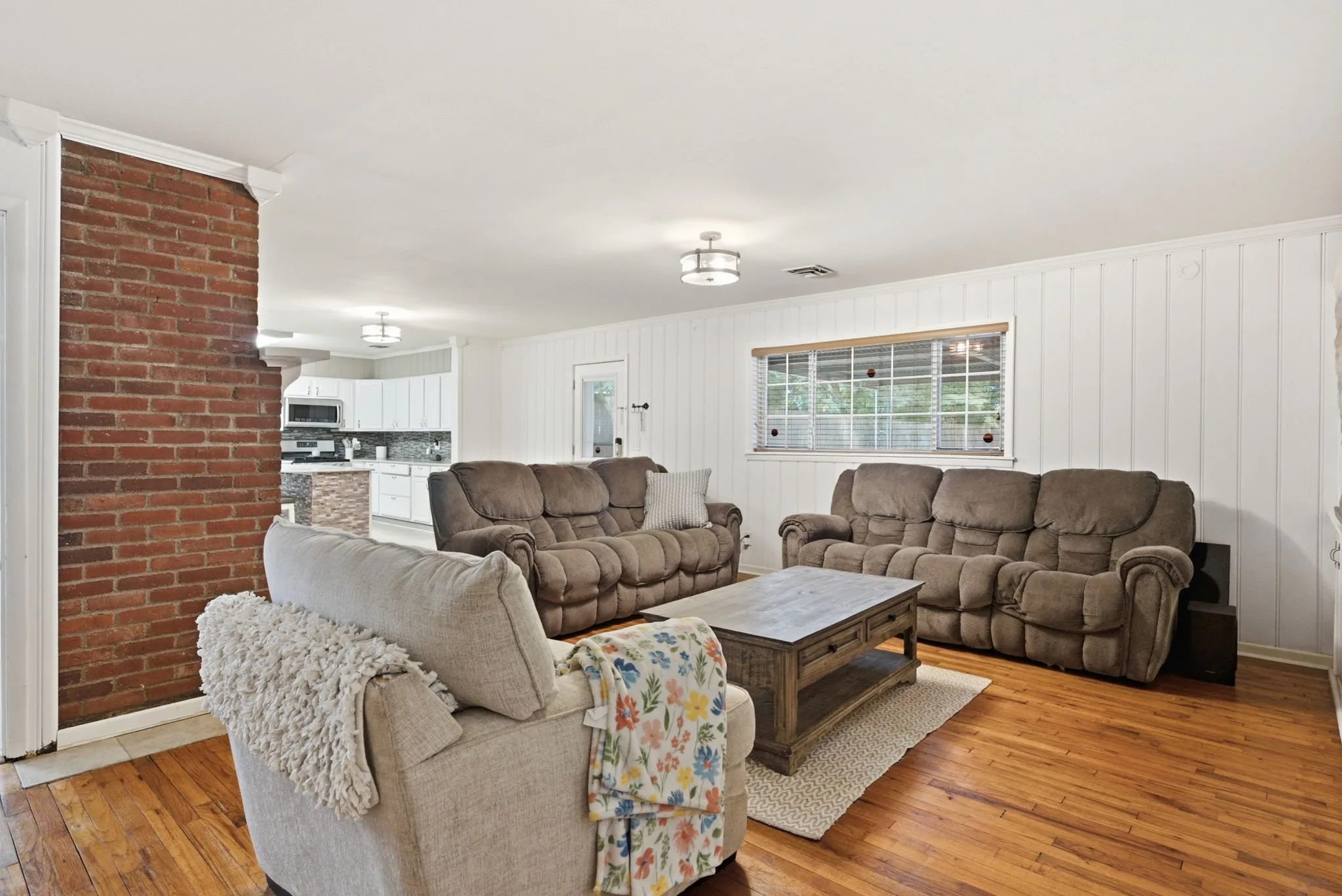 Hardwood flooring, exposed brick architectural element, white paneled wall, recessed lighting, and a large window
