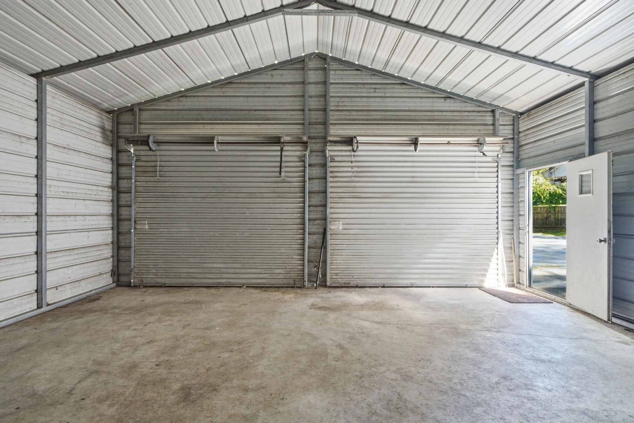 Metal carport structure featuring a concrete floor, two roll-up doors, and an additional side entry door