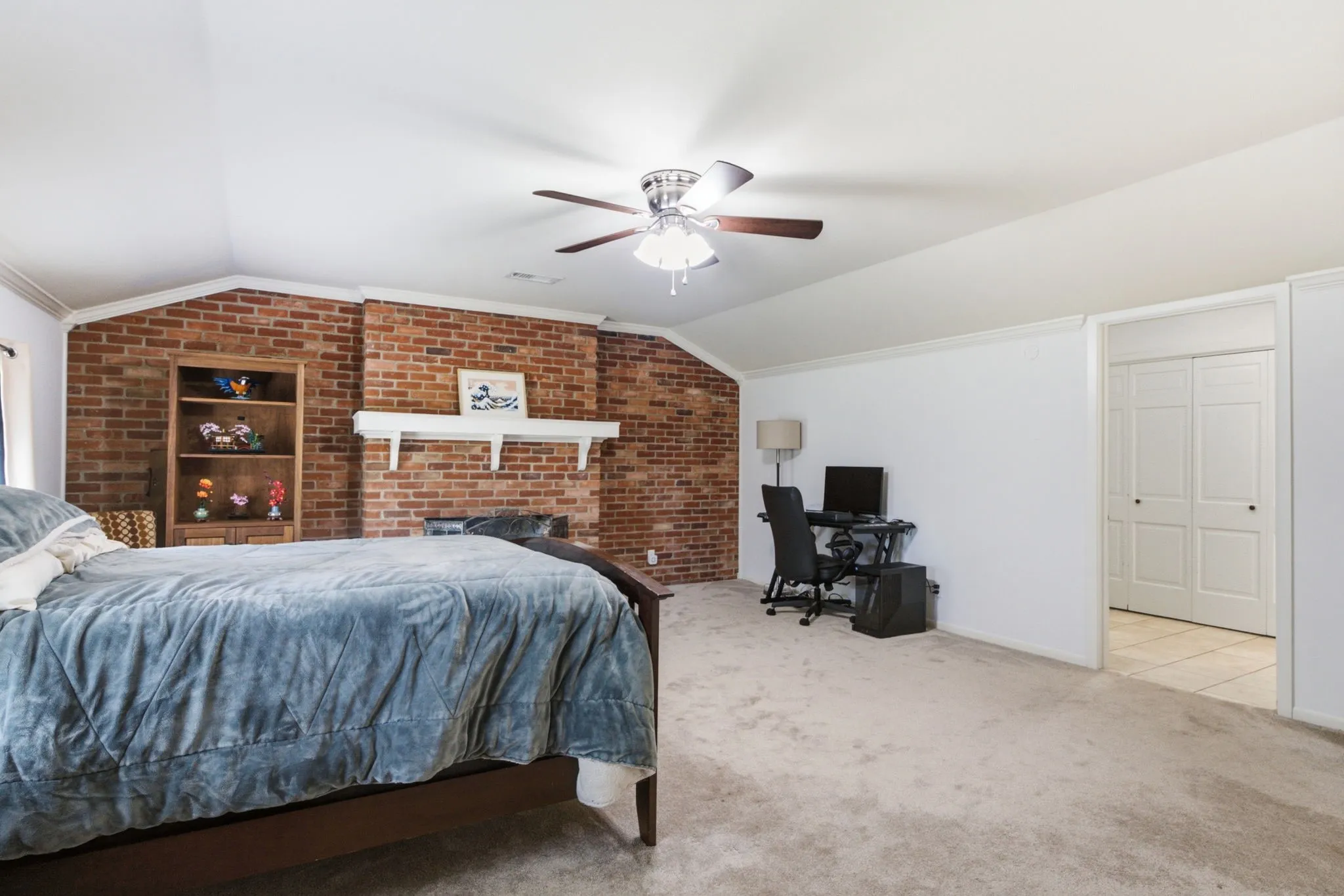 Exposed brick wall with a white mantel, ceiling fan, vaulted ceiling, and built-in shelving