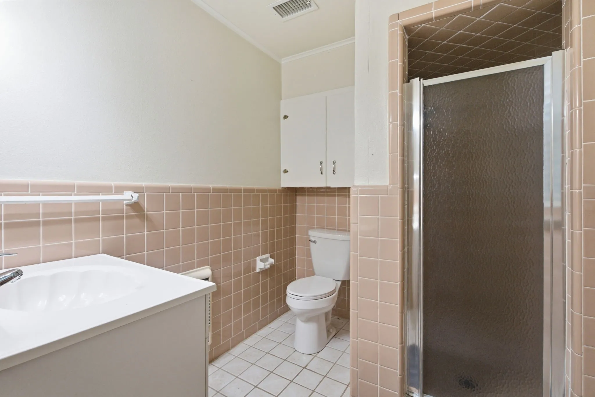 Vanity with an integrated sink, built-in wall cabinetry, tiled shower with glass enclosure, toilet, and tiled flooring