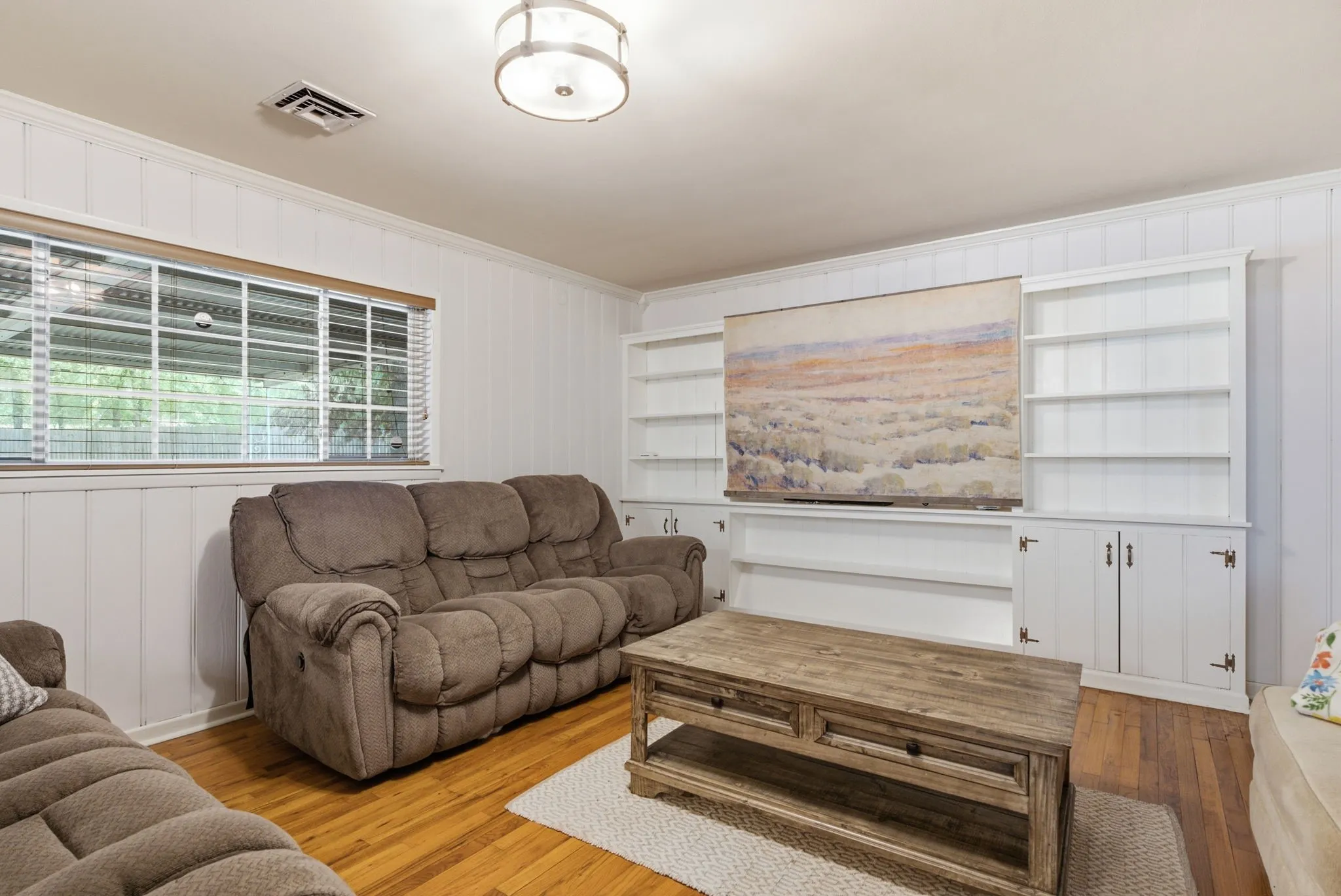 Hardwood flooring, white wall paneling, built-in shelving, white cabinetry, and a flush mount light fixture
