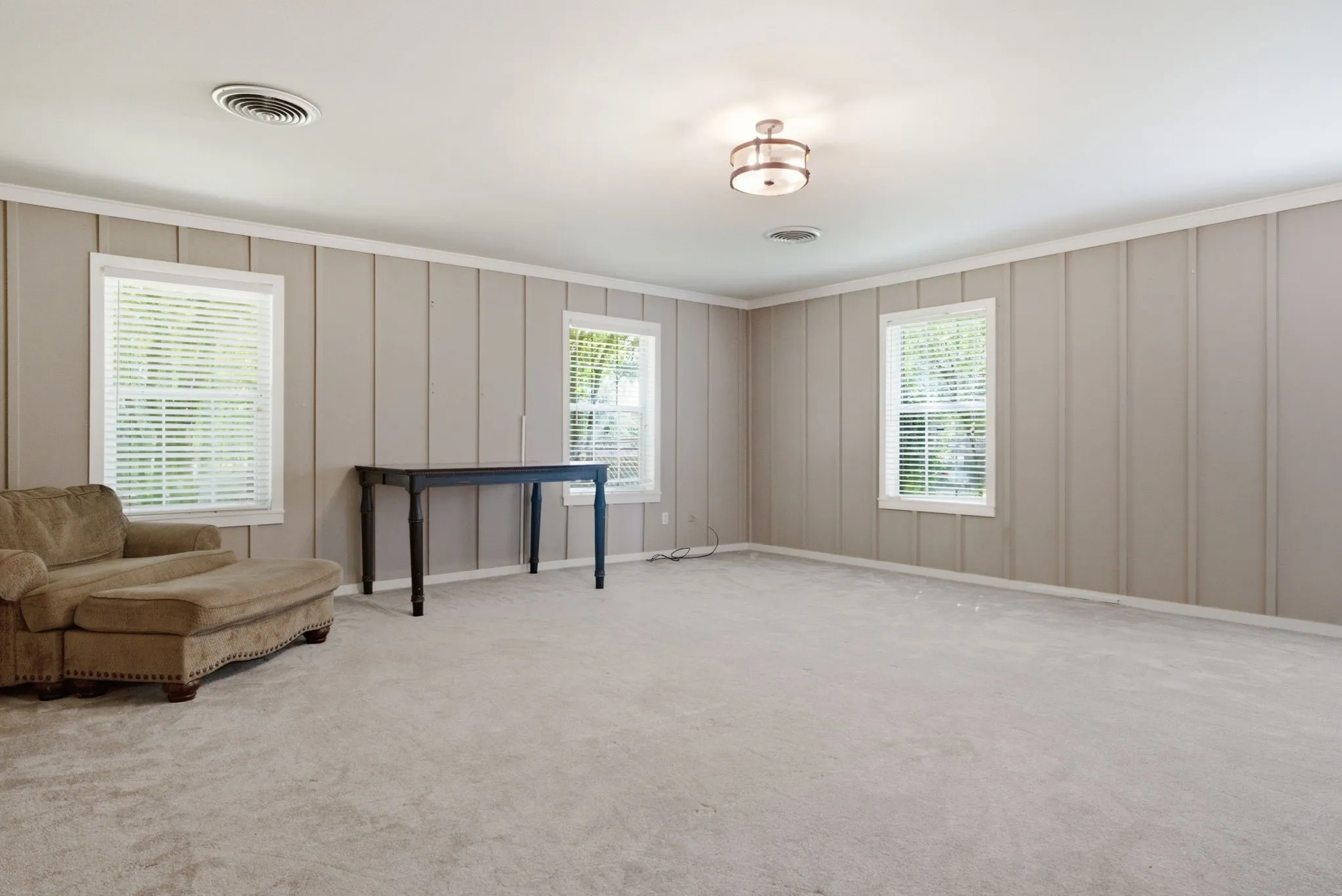 Expansive room featuring carpet flooring, board and batten wall paneling, multiple windows with blinds, and a flush mount light fixture