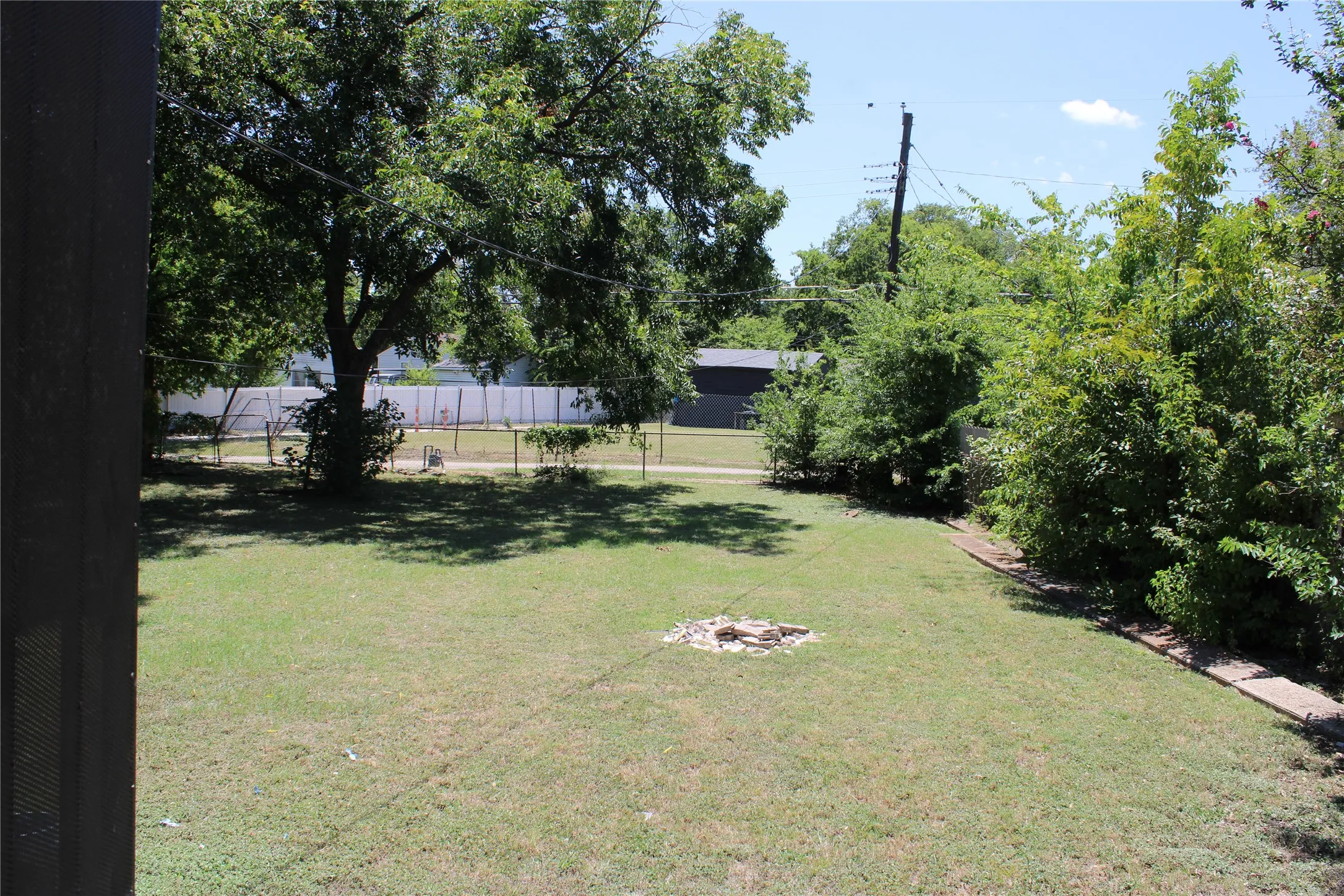 Expansive rear yard featuring a grass lawn, mature trees, and perimeter fencing