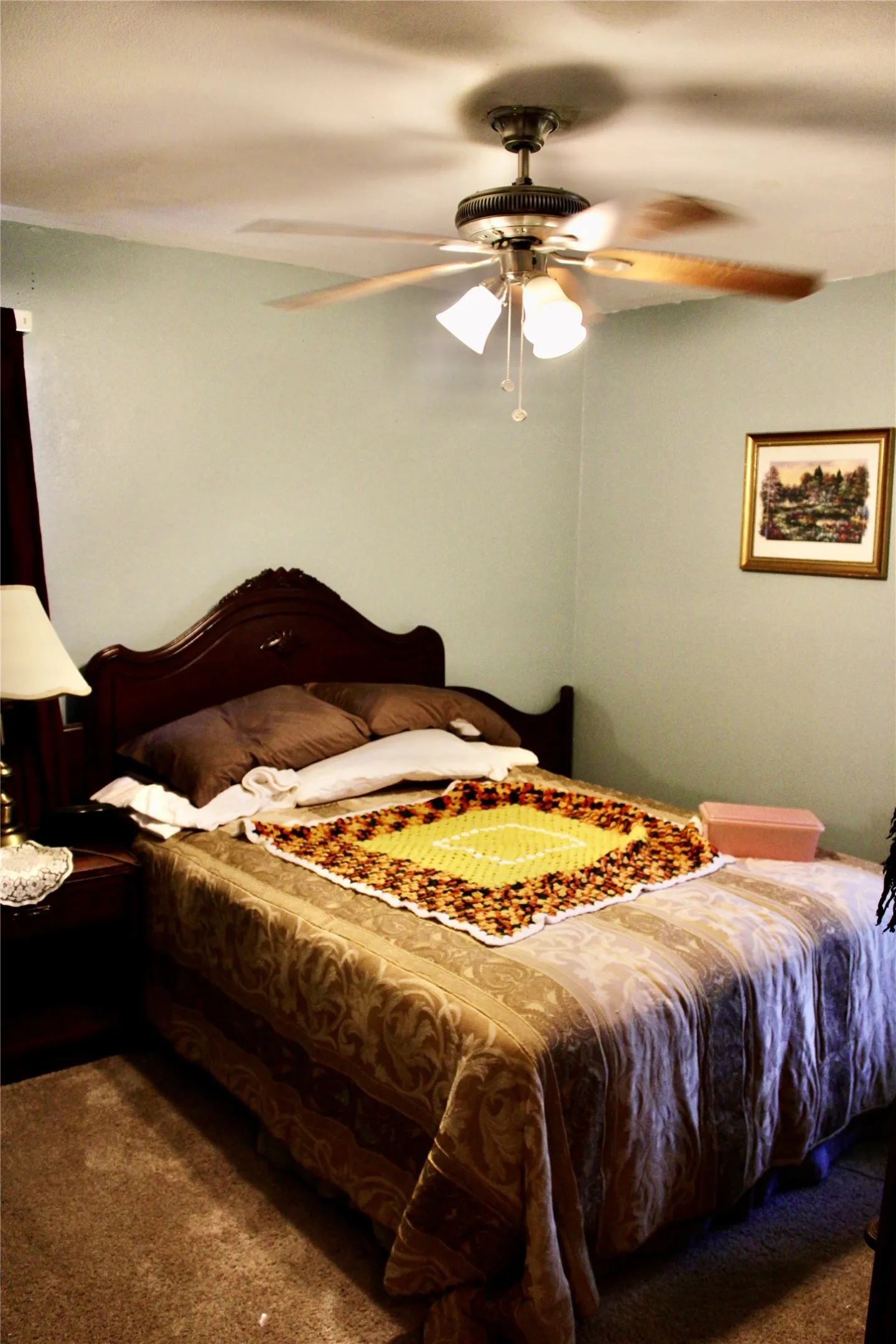 Ceiling fan with integrated lighting, wood-finish headboard, and wall-to-wall carpeting
