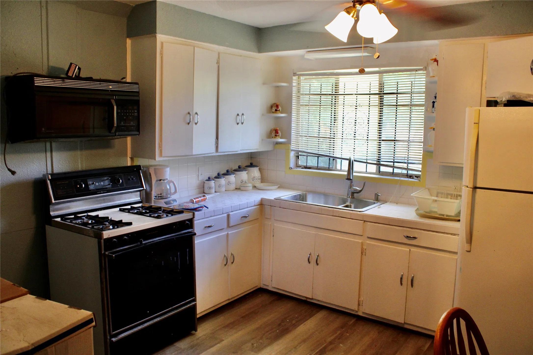 Kitchen featuring a double basin sink, wood-finish flooring, white cabinetry, and an overhead microwave