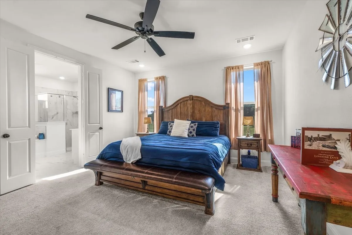 Primary Bedroom: Bright bedroom offers neutral finishes, soft carpeting, a ceiling fan, multiple windows, and direct access to the adjoining bath.