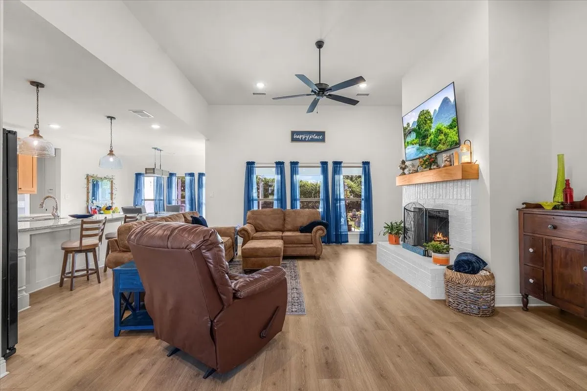 Living Room: Bright gathering space offers a vaulted ceiling, fireplace with raised hearth and wood mantel, and multiple windows providing natural light.