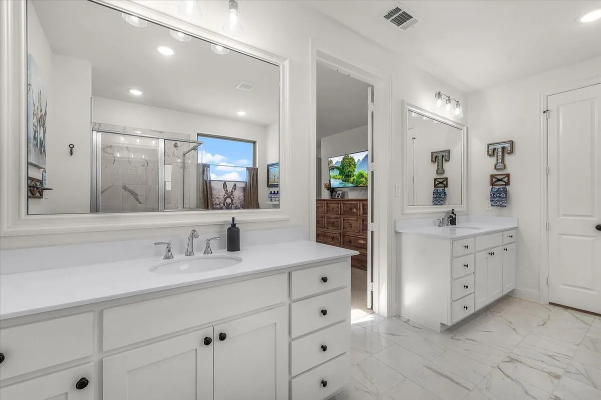 Primary Bathroom: Dual vanity areas with expansive mirrors, white cabinetry, and marble-look flooring provide generous counter and storage space.