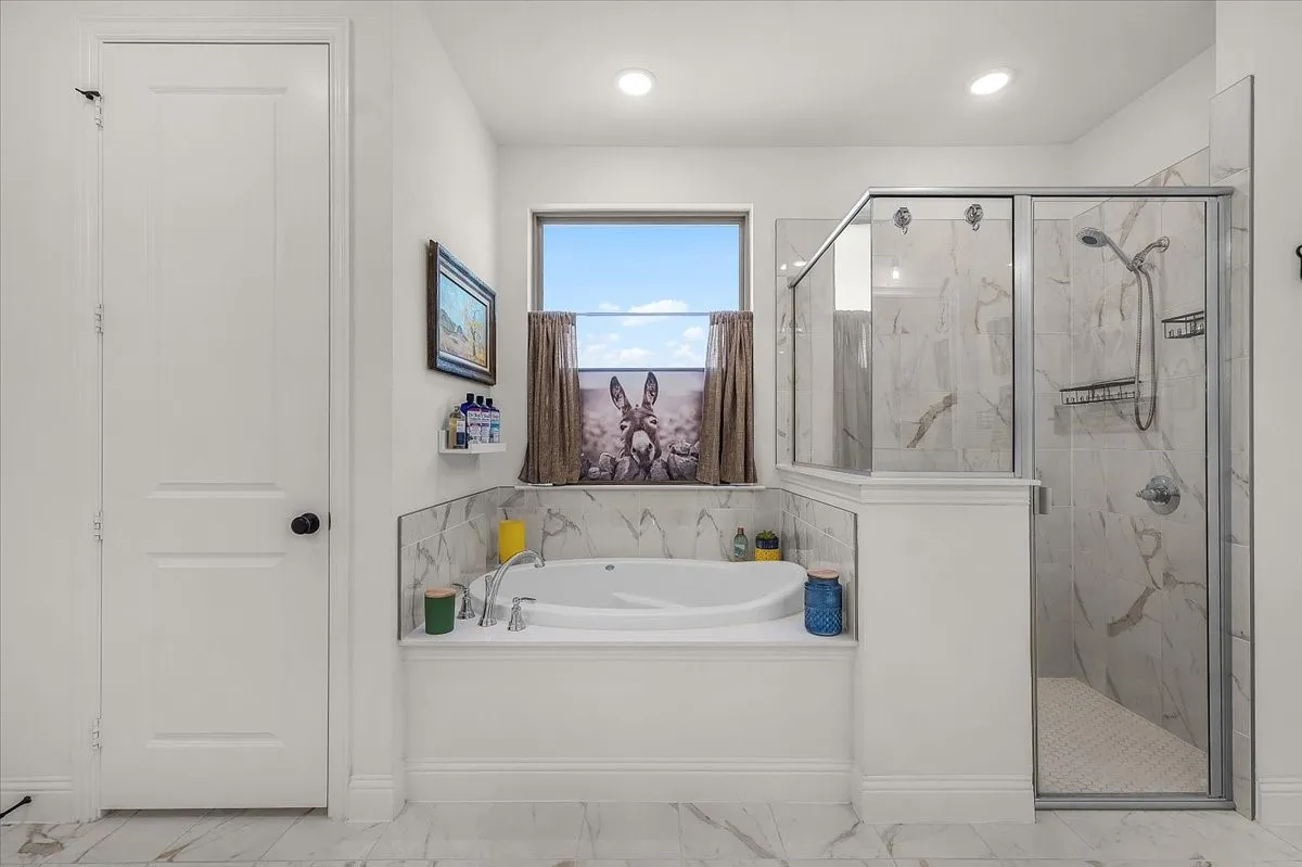 Primary Bathroom: Soaking tub and separate glass-enclosed shower feature coordinating marble-look tile for a bright, cohesive finish.