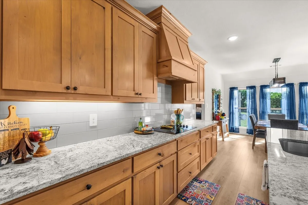 Kitchen: Warm wood cabinetry, light stone countertops, subway-style backsplash, and a substantial vent hood create a cohesive kitchen workspace.