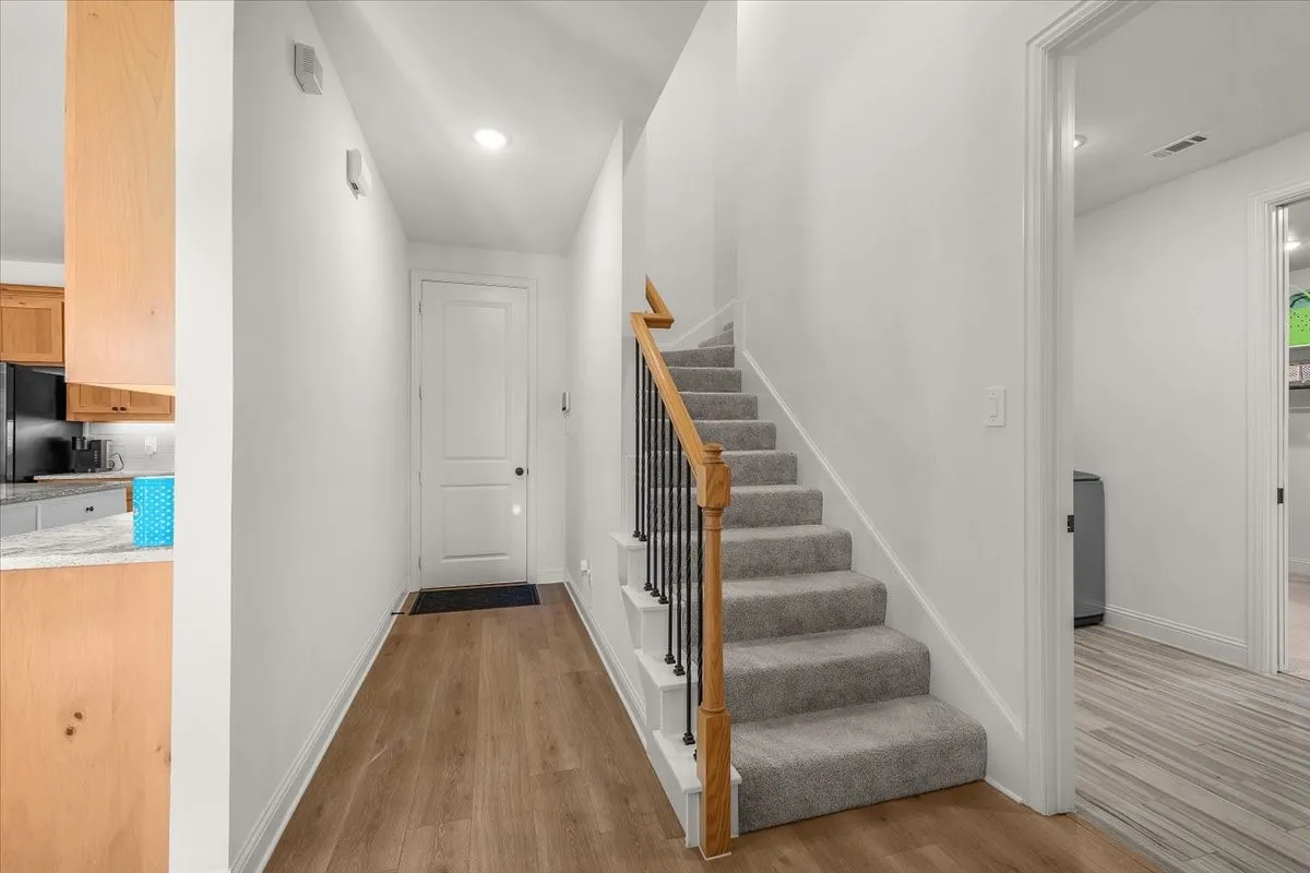 Stairway: Carpeted staircase features a wood handrail with dark metal balusters and connects seamlessly with the wood-look flooring below.
