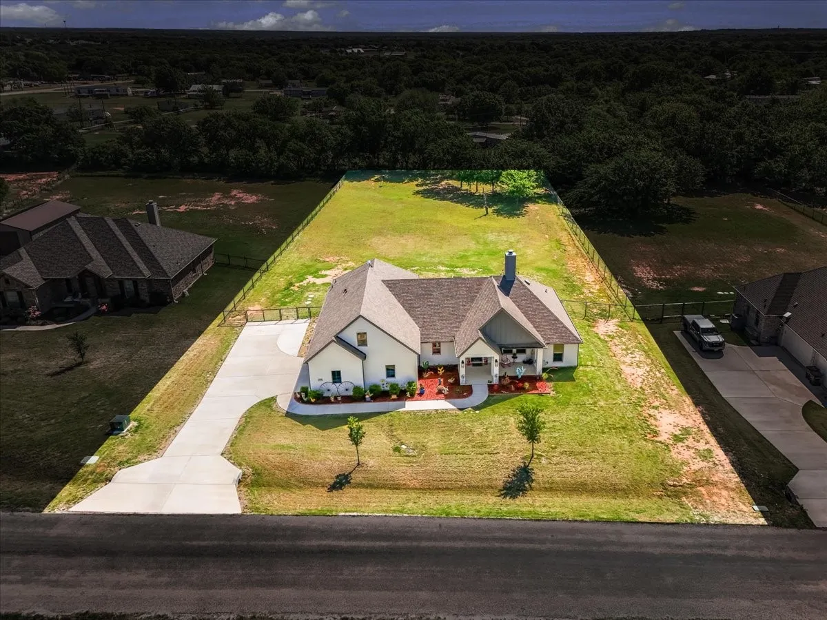 Aerial Exterior: Overhead view emphasizes the home’s placement on the property, broad lawn areas, driveway, and fenced perimeter.