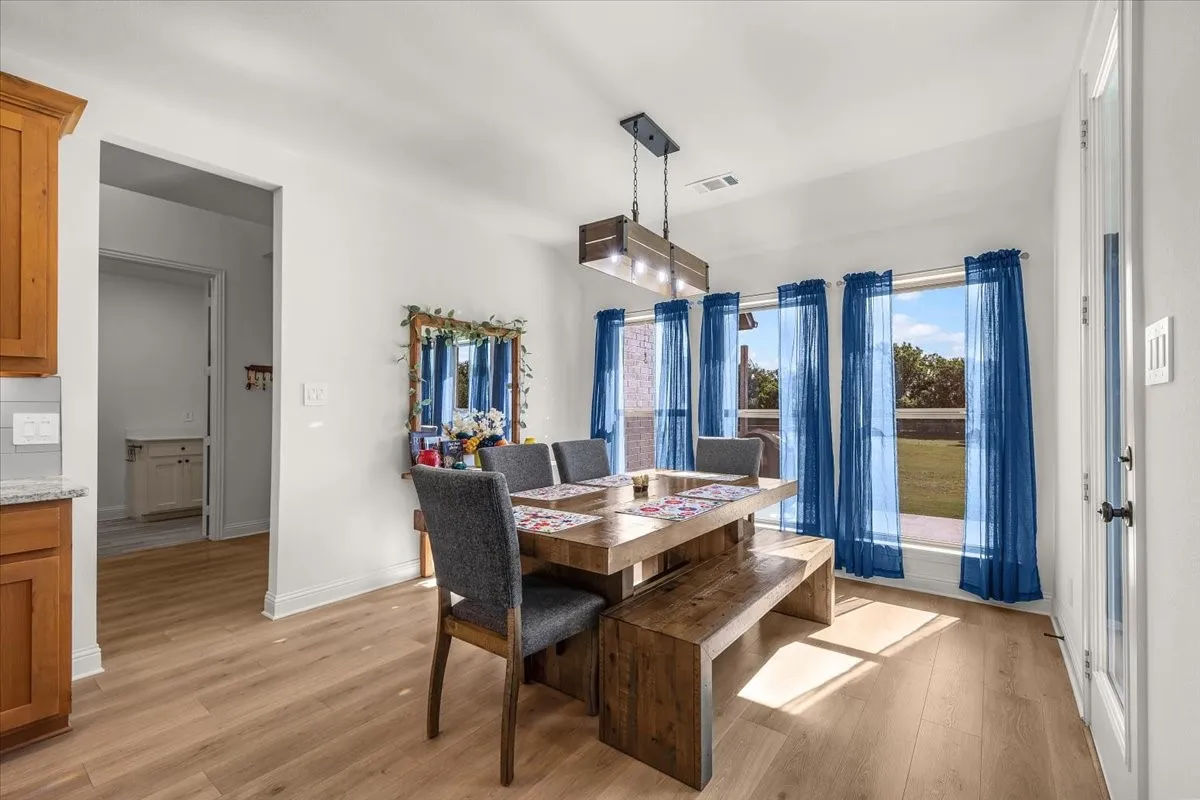 Dining Area: Sunlit dining space features generous windows, wood-look flooring, a statement light fixture, and convenient adjacency to the kitchen.