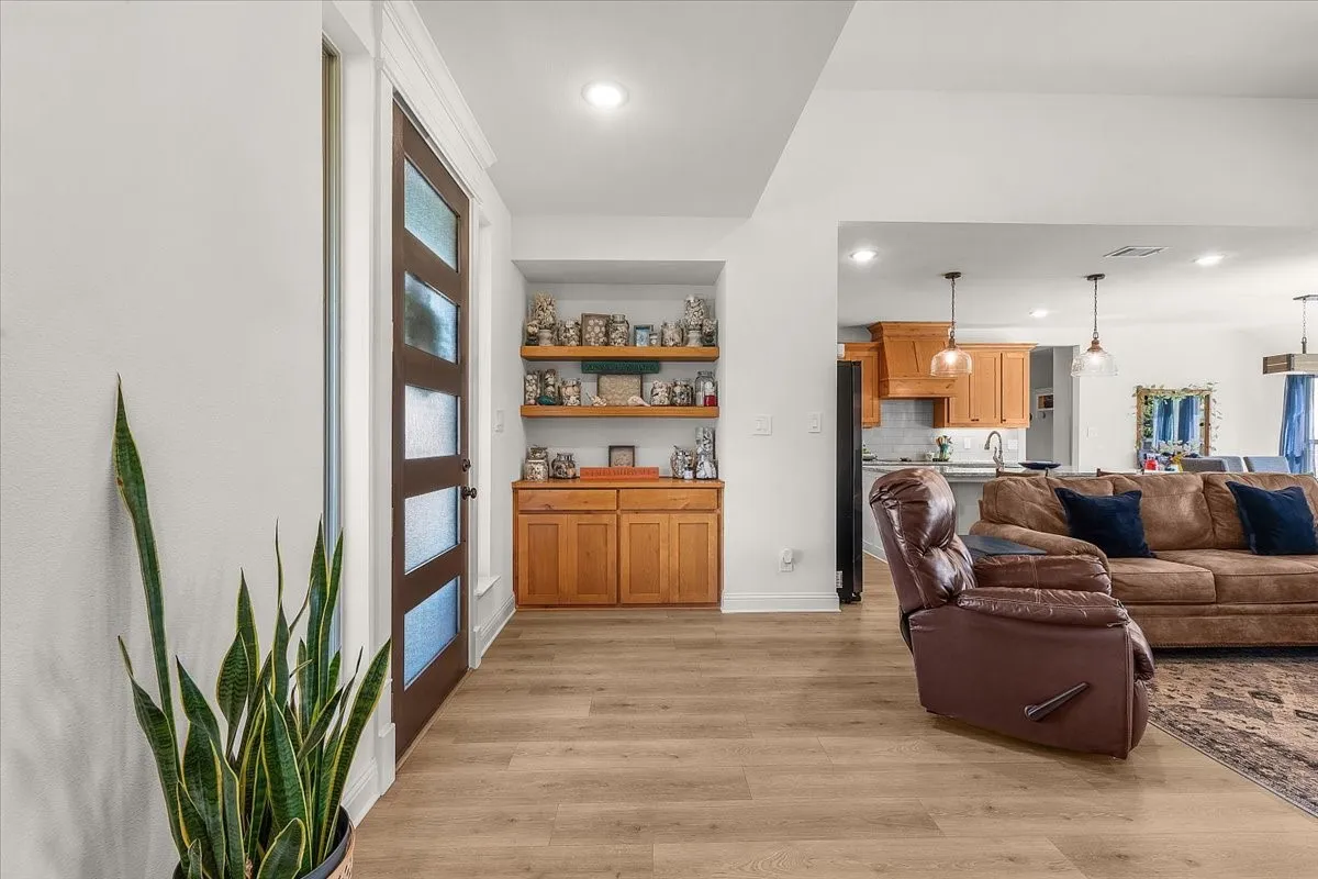 Entry: Modern glass-panel front door opens to an airy interior with wood-look flooring, built-in cabinetry, and an open connection to the main living spaces.