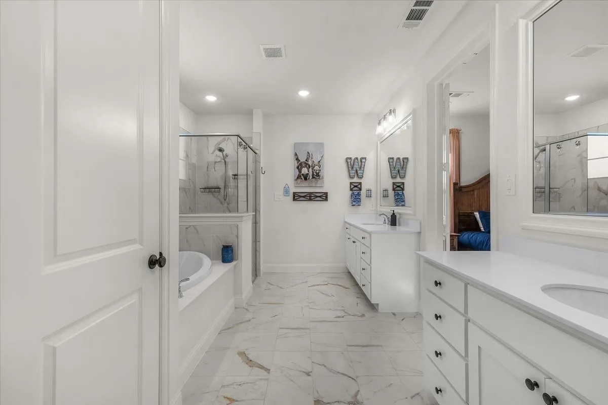 Primary Bathroom: Spacious bath features dual vanities, a soaking tub, glass-enclosed shower, marble-look surfaces, and abundant recessed lighting.