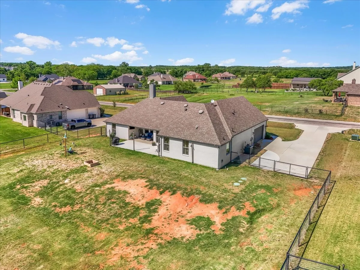 Aerial view of this Springtown home highlighting the expansive fenced lot, extended driveway, mature trees and surrounding property.