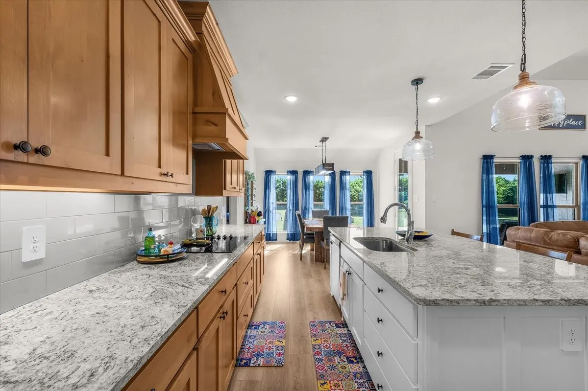 Kitchen: Long stretches of cabinetry and stone countertops frame the generous center island, with clear sightlines into the adjoining dining and living spaces.