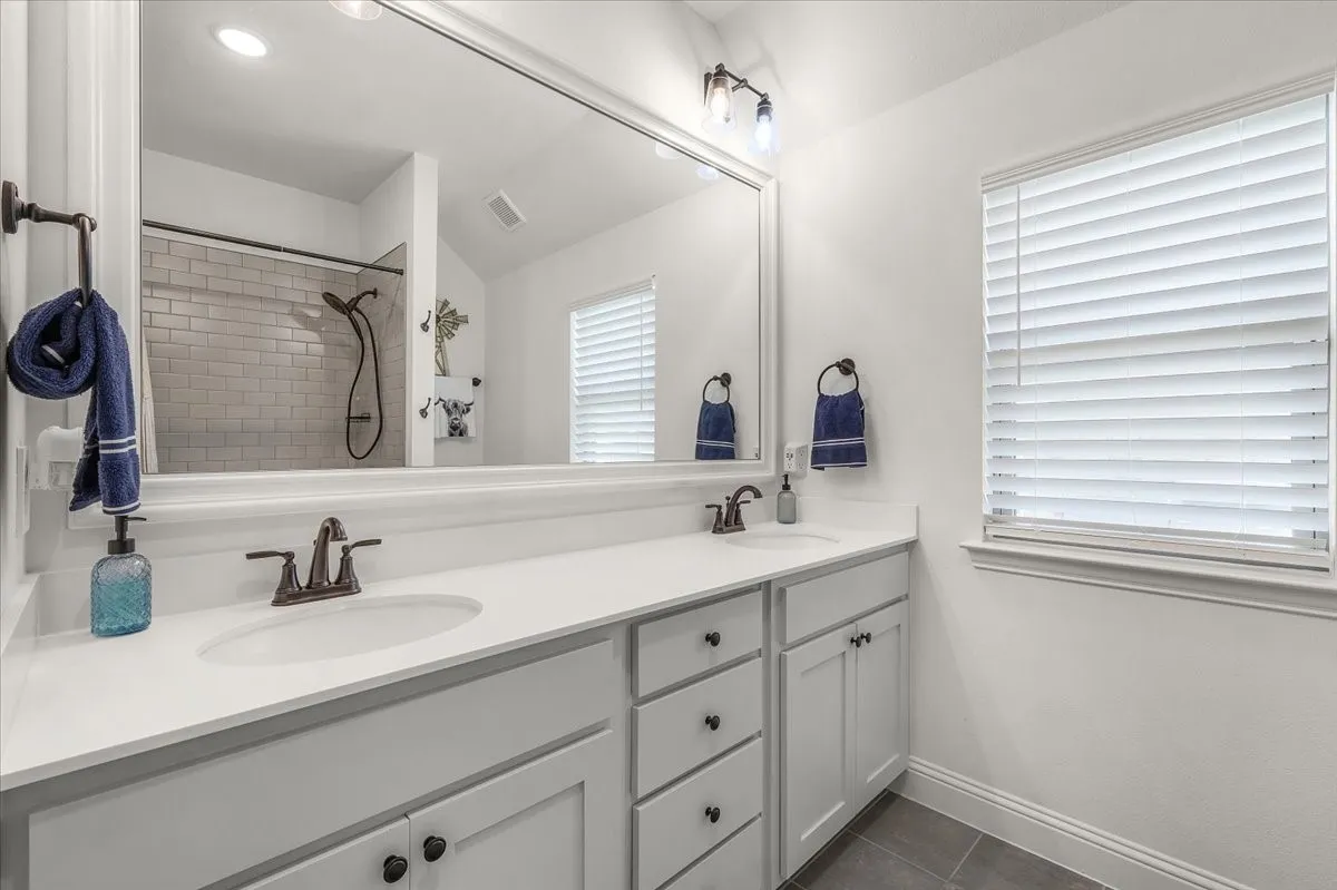 Bathroom: Dual-sink vanity provides ample counter and cabinet space, complemented by a large mirror, window, and tiled shower.