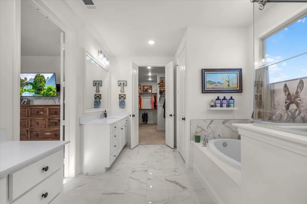 Primary Bathroom: Light-filled bath combines a soaking tub, vanity storage, marble-look flooring, and convenient access to the adjoining closet.