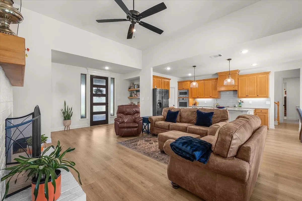 Living Room: Spacious open-concept living area features a vaulted ceiling, fireplace, wood-look flooring, and direct sightlines into the kitchen.