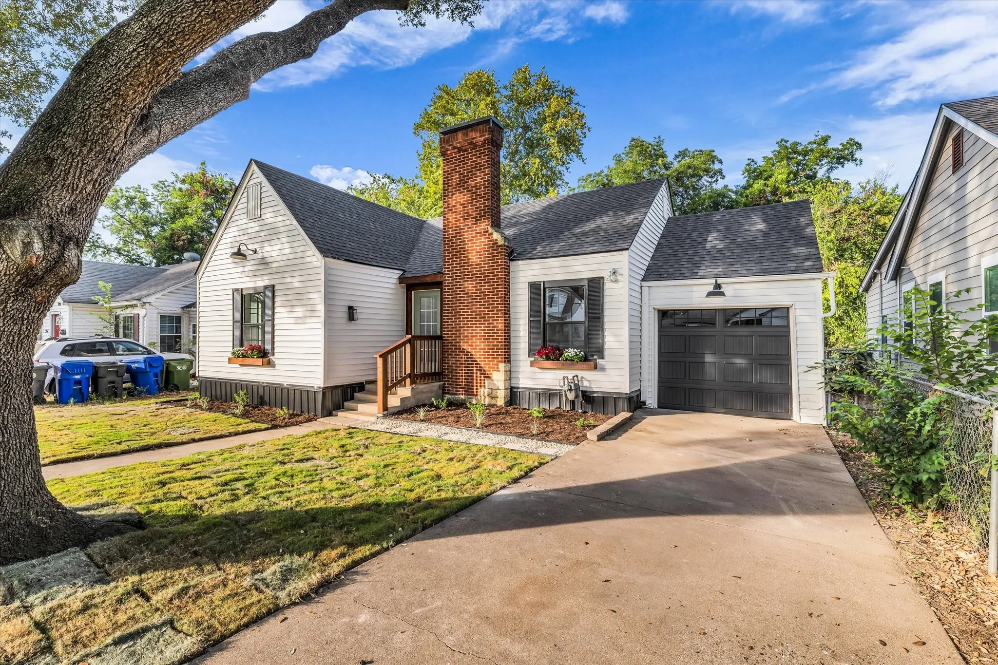 White siding exterior with a dark shingle roof, brick chimney, and a dark garage door