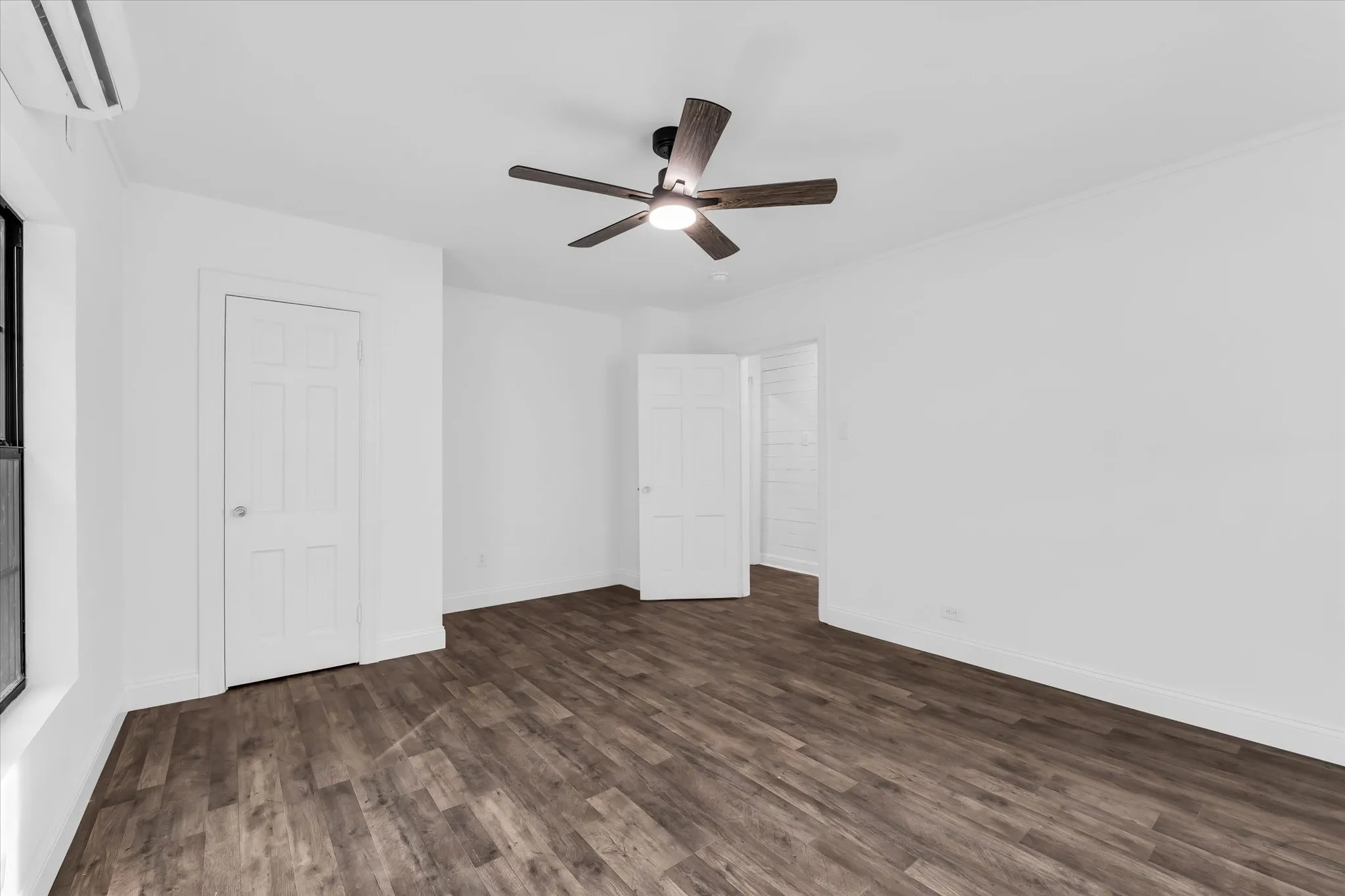 Wood-finish flooring, white walls, ceiling fan with integrated lighting, and white paneled doors