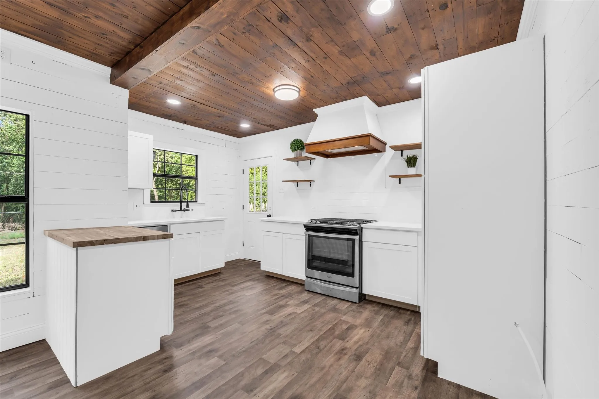 Wood-finish ceiling beams, wood-finish flooring, white shiplap walls, white cabinetry, and stainless steel range