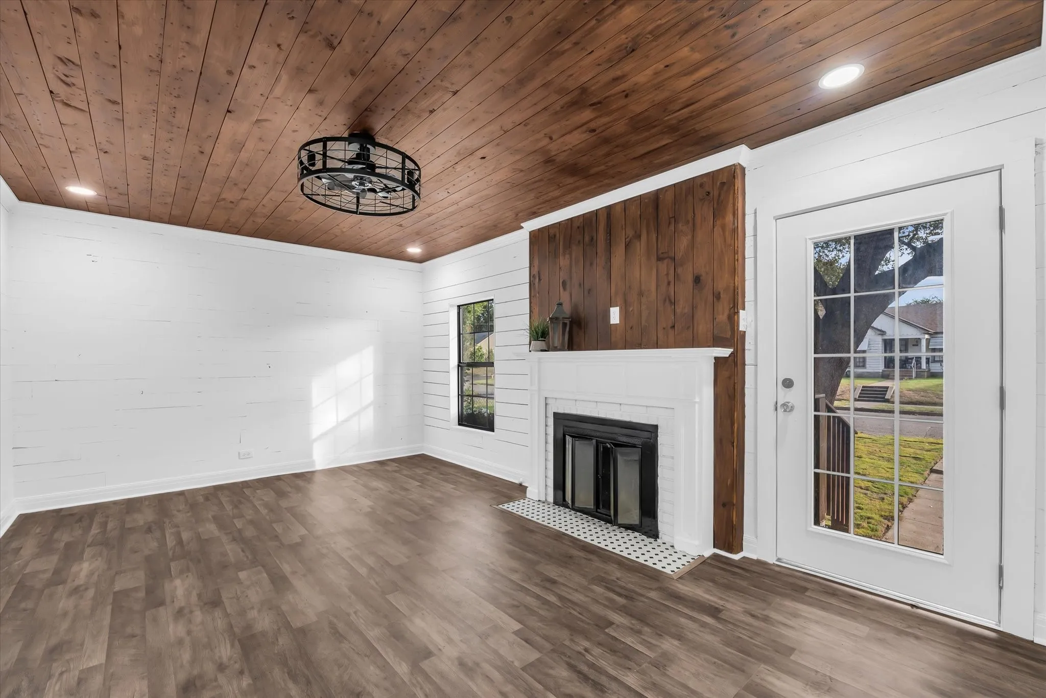 Wood-finish ceiling, wood-finish flooring, white shiplap walls, white fireplace with hearth, and a glass-paneled door