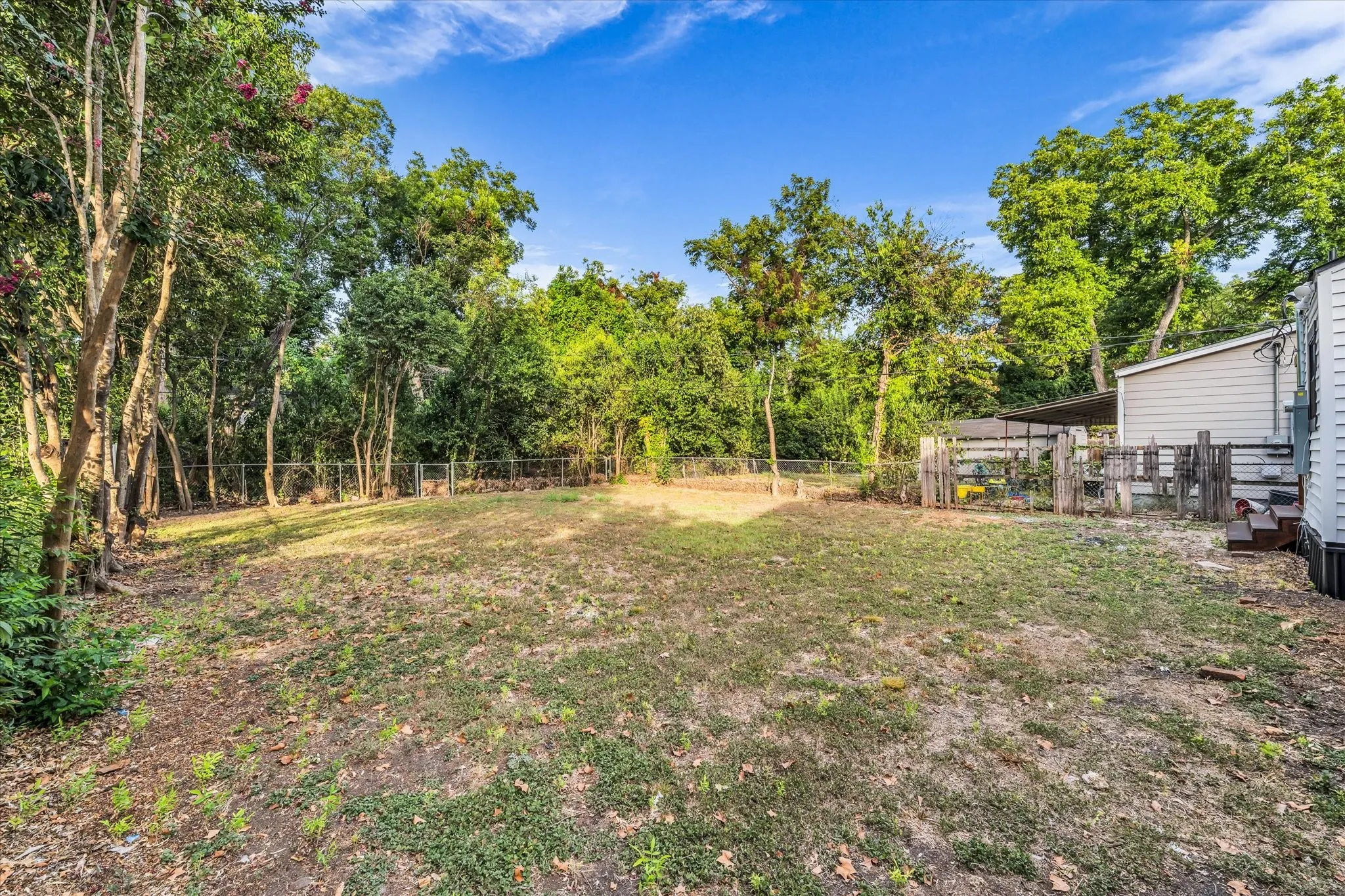 Expansive backyard with a chain-link fence, mature trees, and a detached structure
