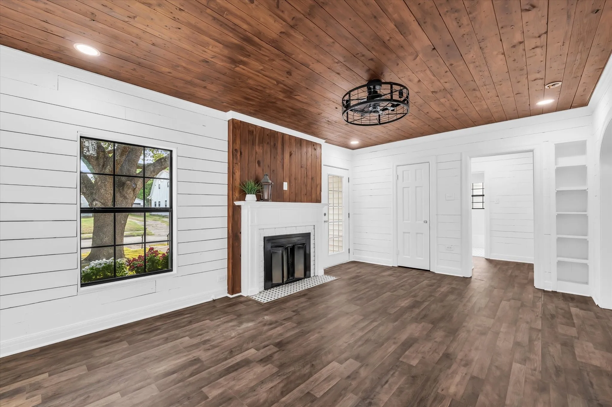 Wood-finish flooring, white shiplap walls, wood plank ceiling, fireplace with tile hearth, and built-in shelving