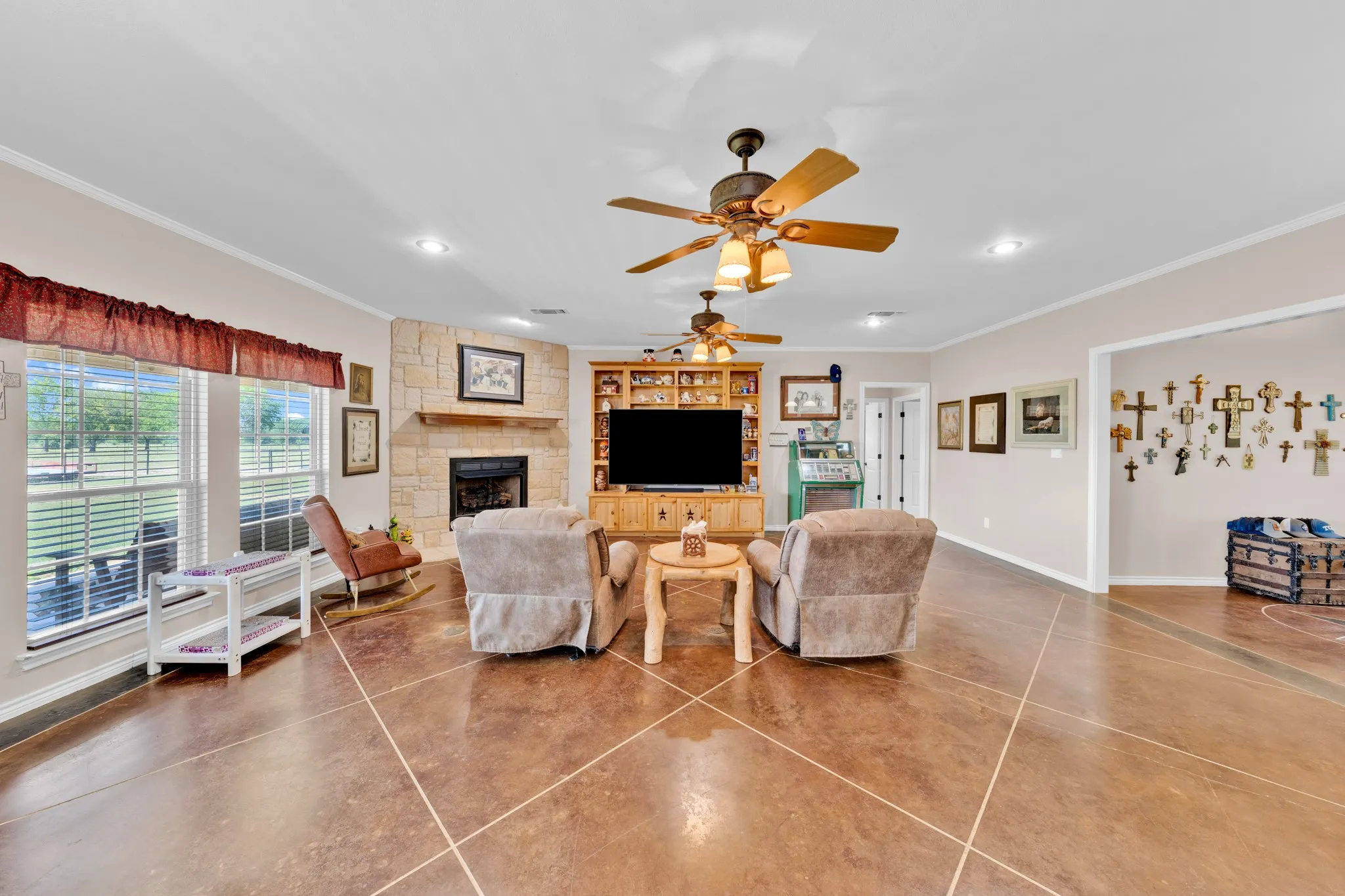 Expansive living area featuring a stone-clad fireplace with a wood mantel, multiple ceiling fans, recessed lighting, and large windows