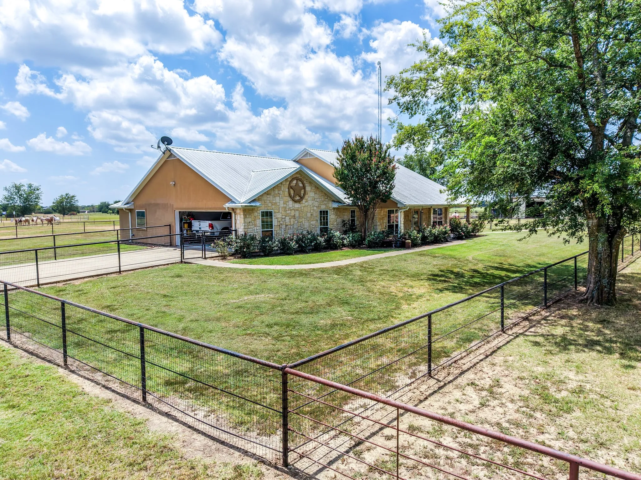 Stone and stucco exterior, metal roof, attached garage, fenced perimeter, and mature trees